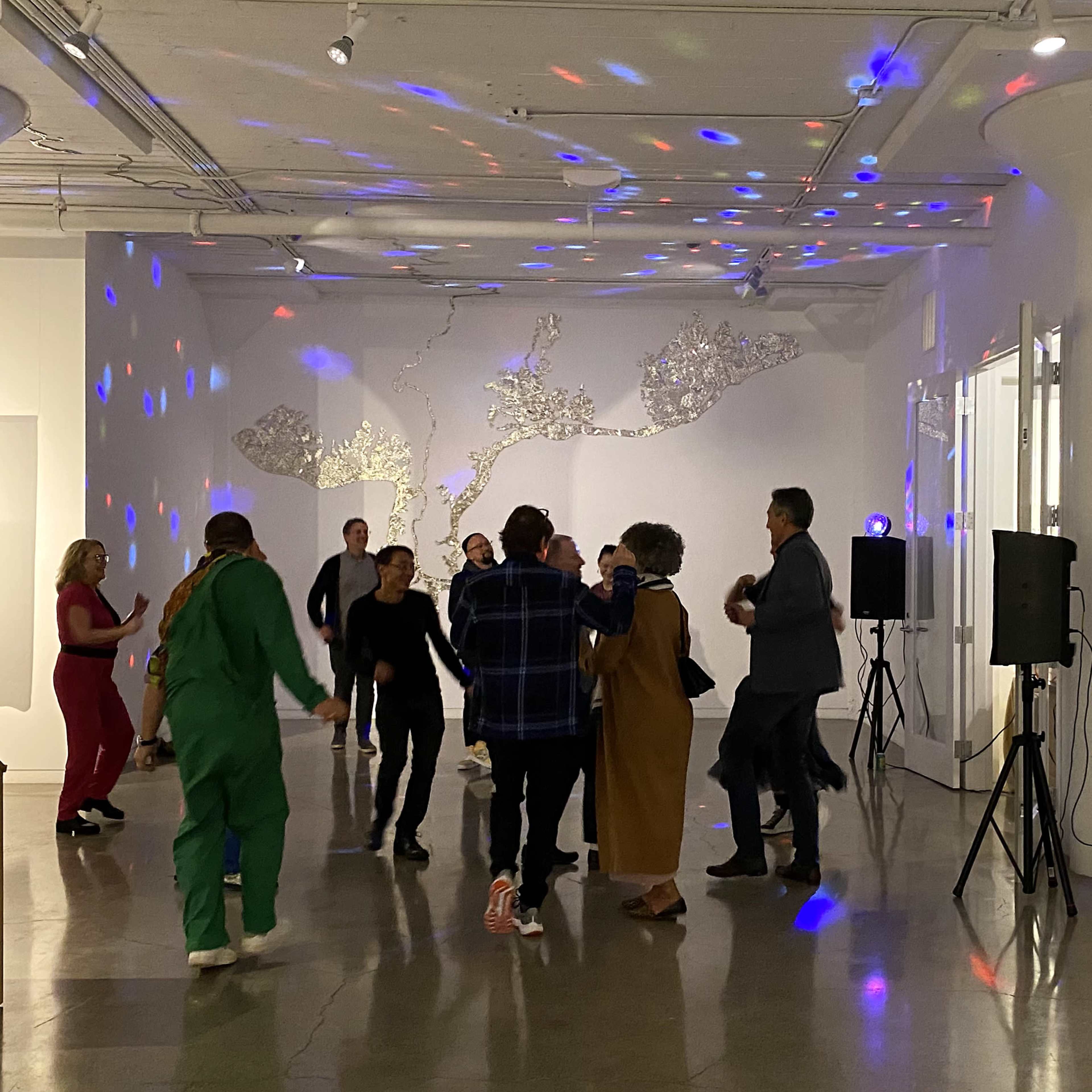 A group of people dance in a gallery while colorful lights reflect on the walls.