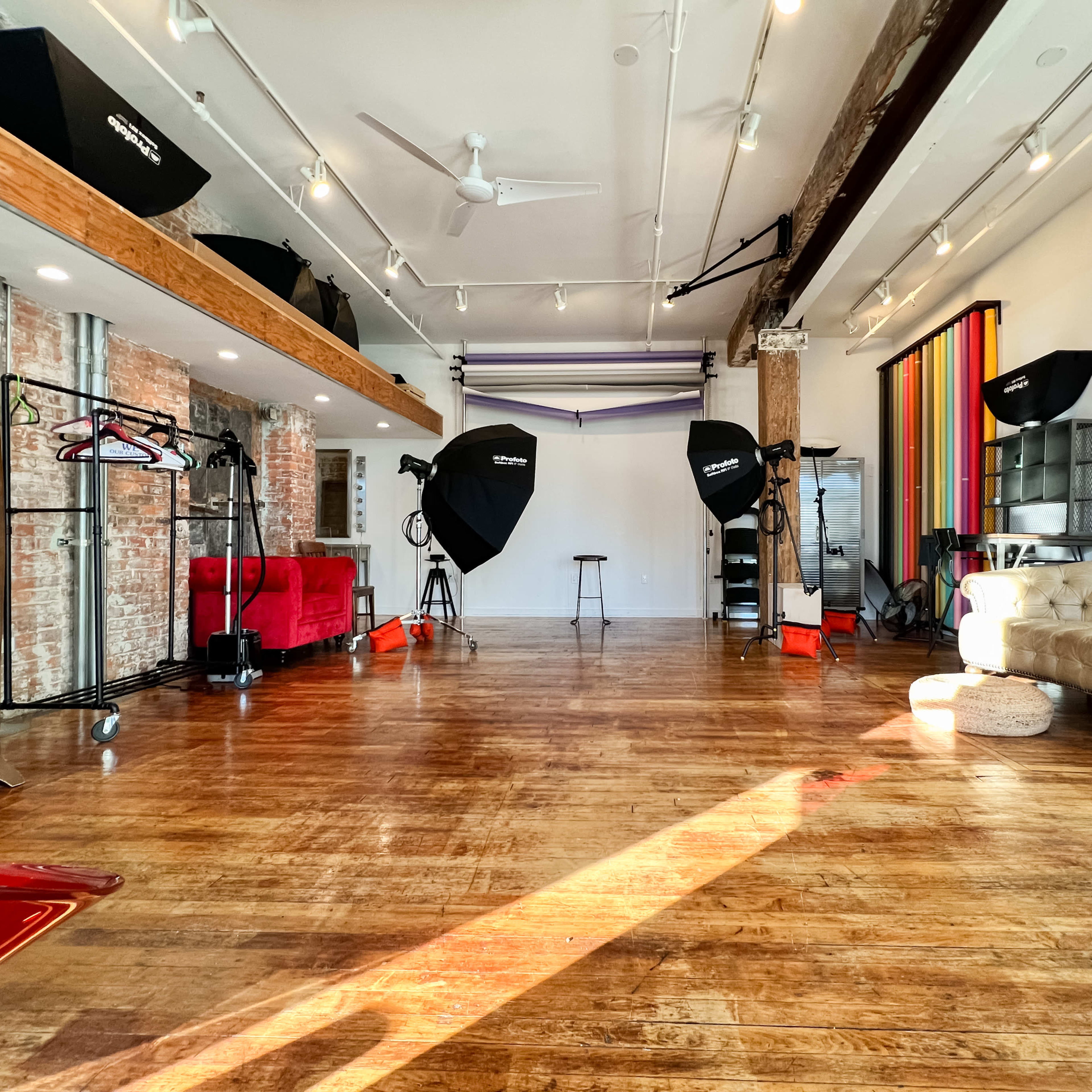 A photography studio featuring a hardwood floor, backdrops, lighting equipment, and furniture arranged in an open space.
