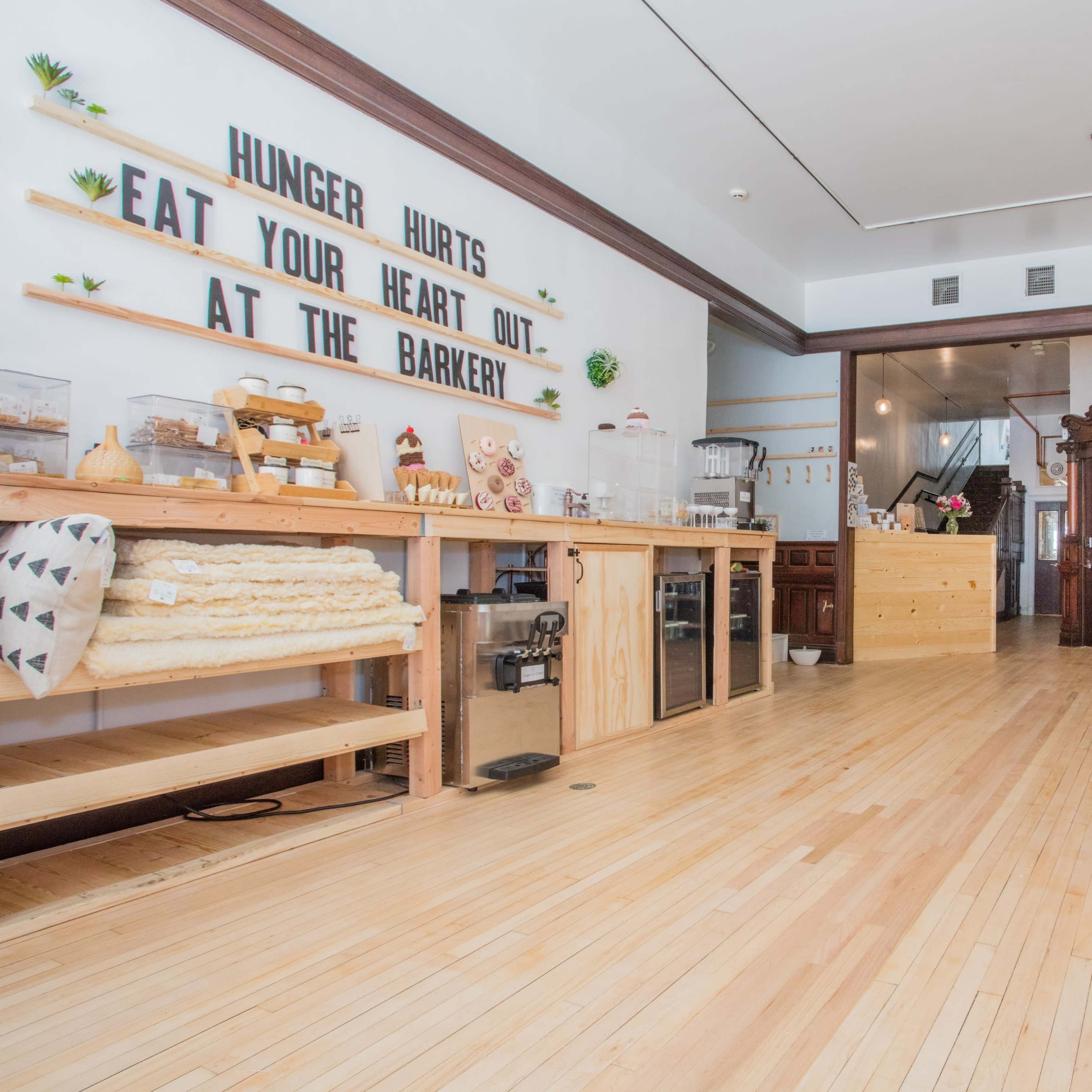 The interior of a pet bakery features wooden counters, a spacious floor, and signage with playful phrases on the walls.