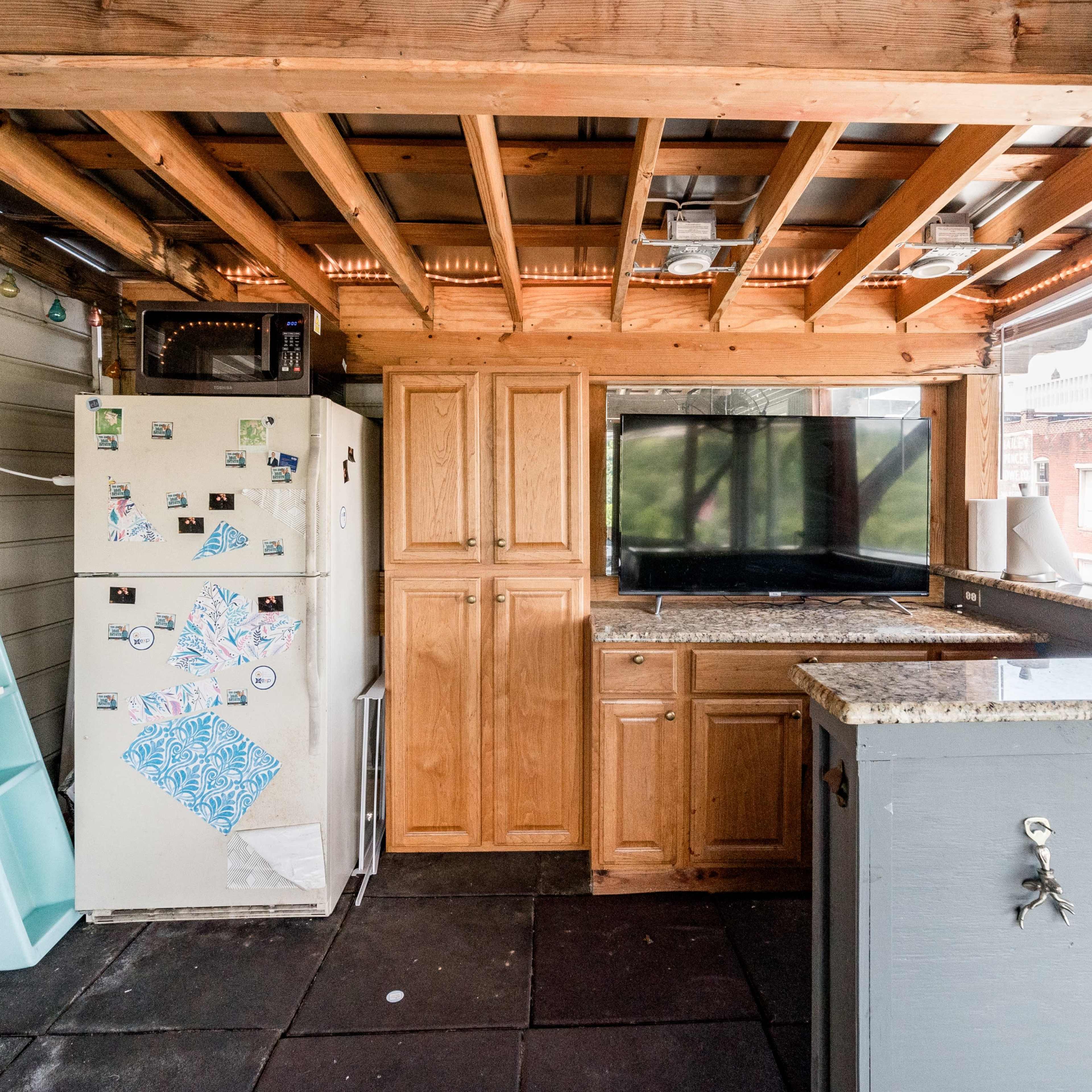 A rustic kitchen space with wooden beams, a refrigerator, cabinets, a sink, and a television mounted on the wall.