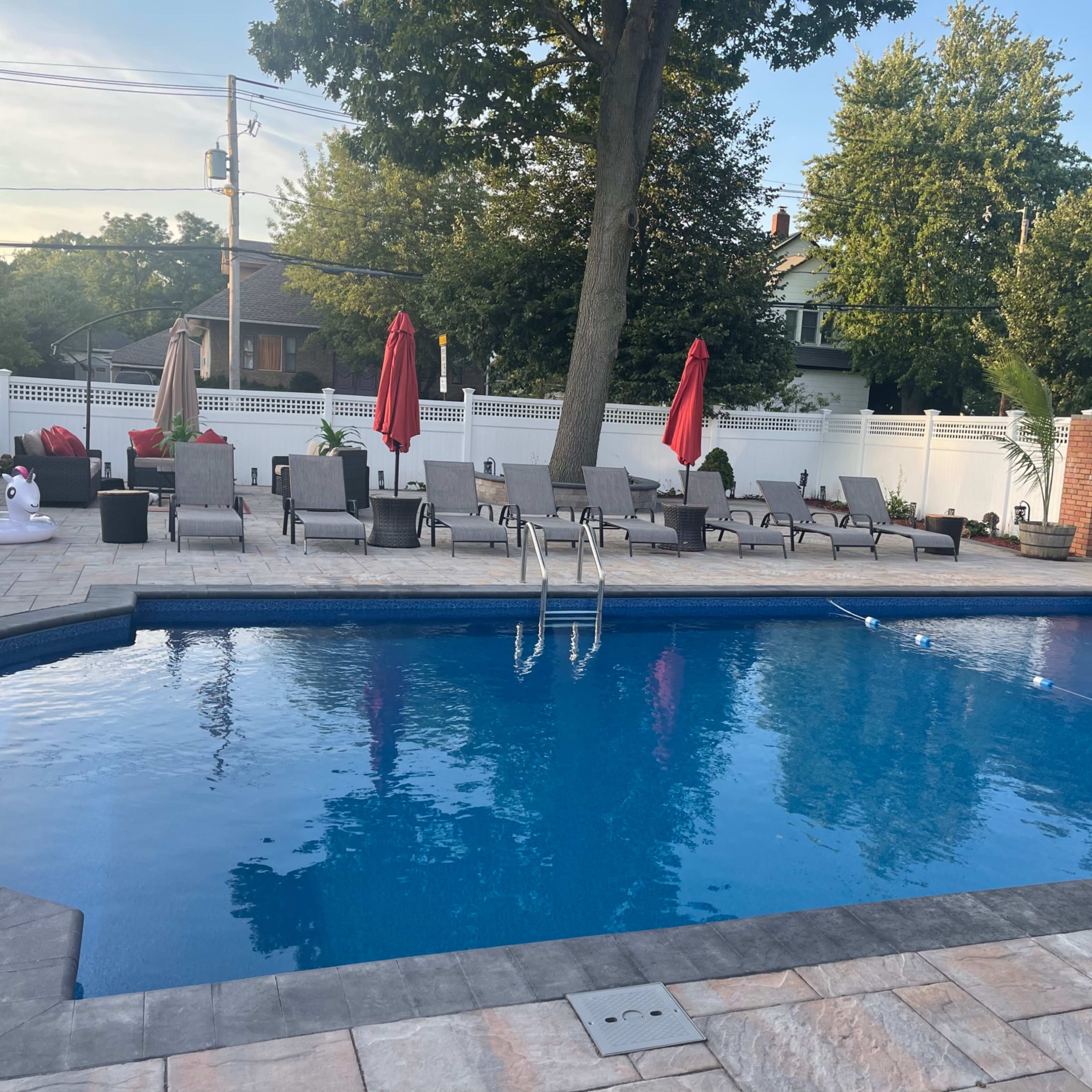 A swimming pool surrounded by lounge chairs and umbrellas in a backyard setting.