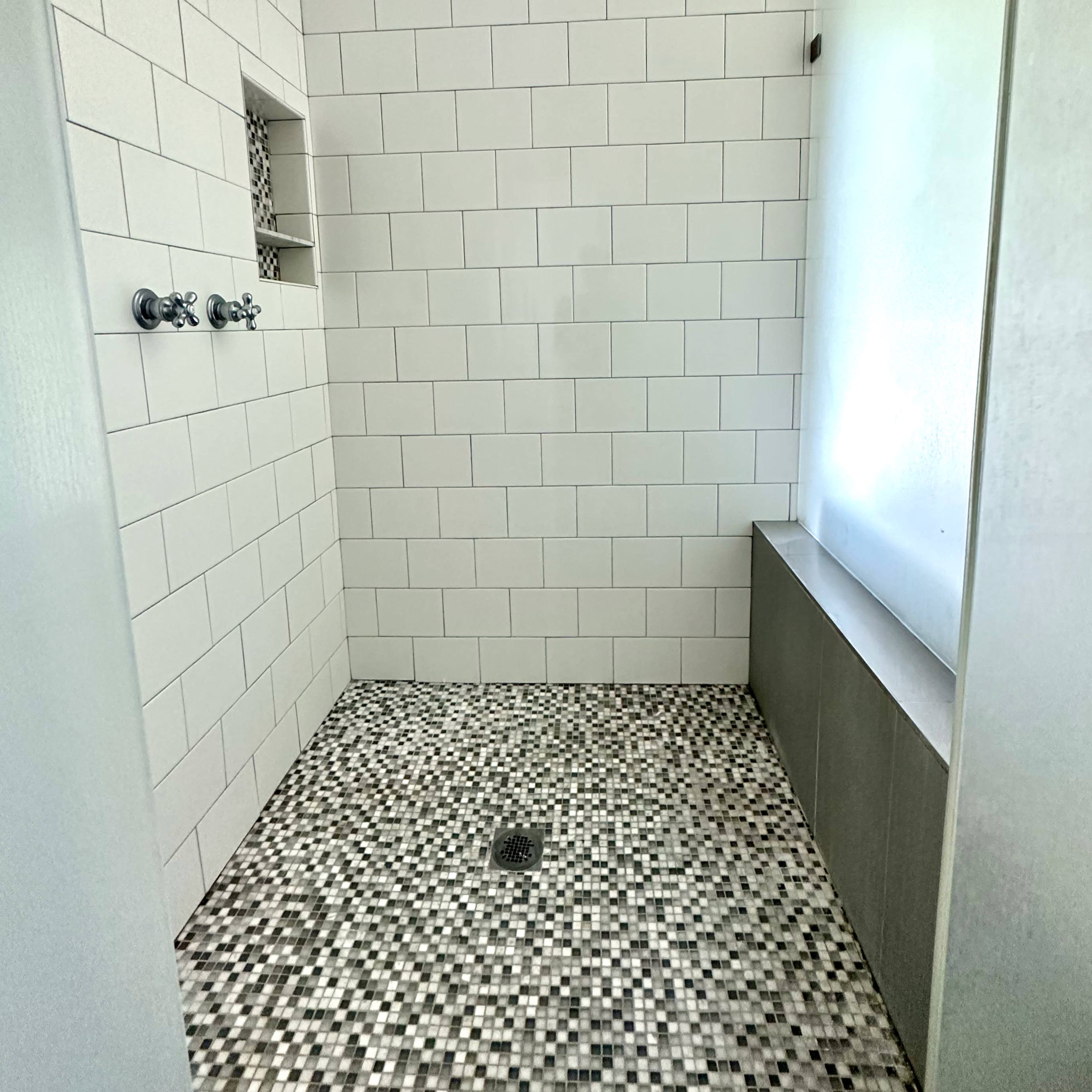 A modern shower space featuring white tiled walls, a mosaic floor, and a glass partition.