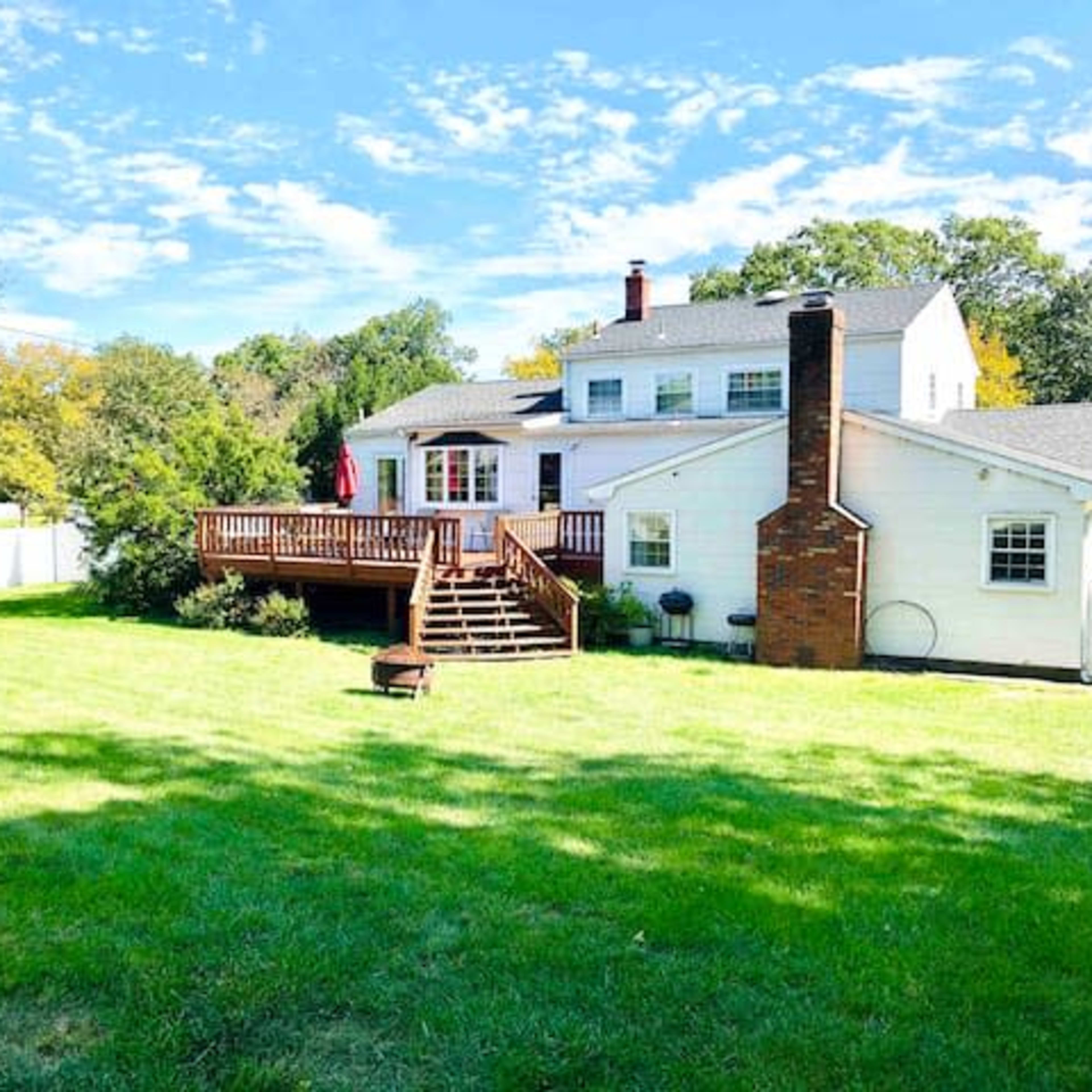 A spacious backyard with a green lawn and a wooden deck attached to a two-story white house.