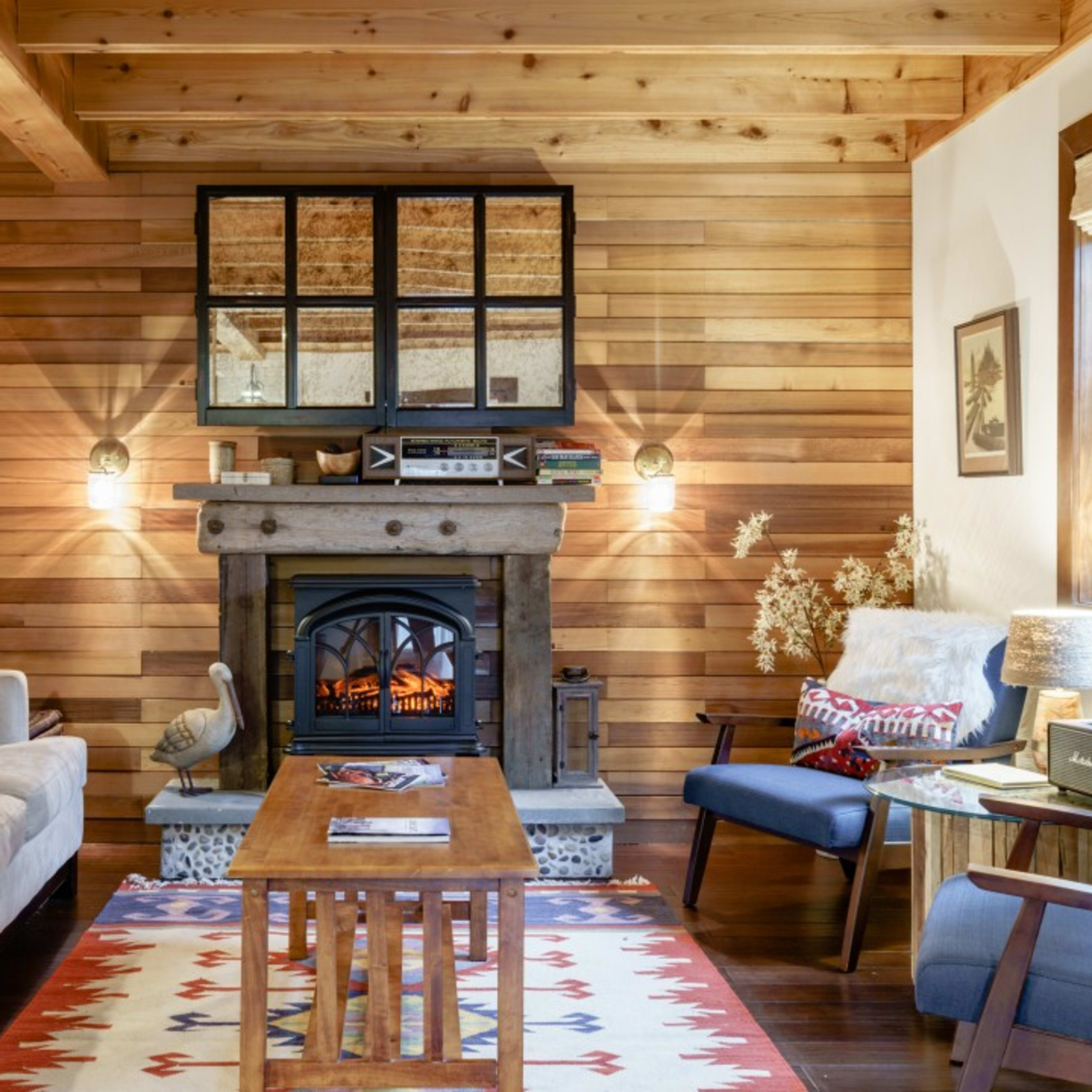 A cozy living room with wooden walls, a fireplace, and a wooden coffee table surrounded by various seating options.