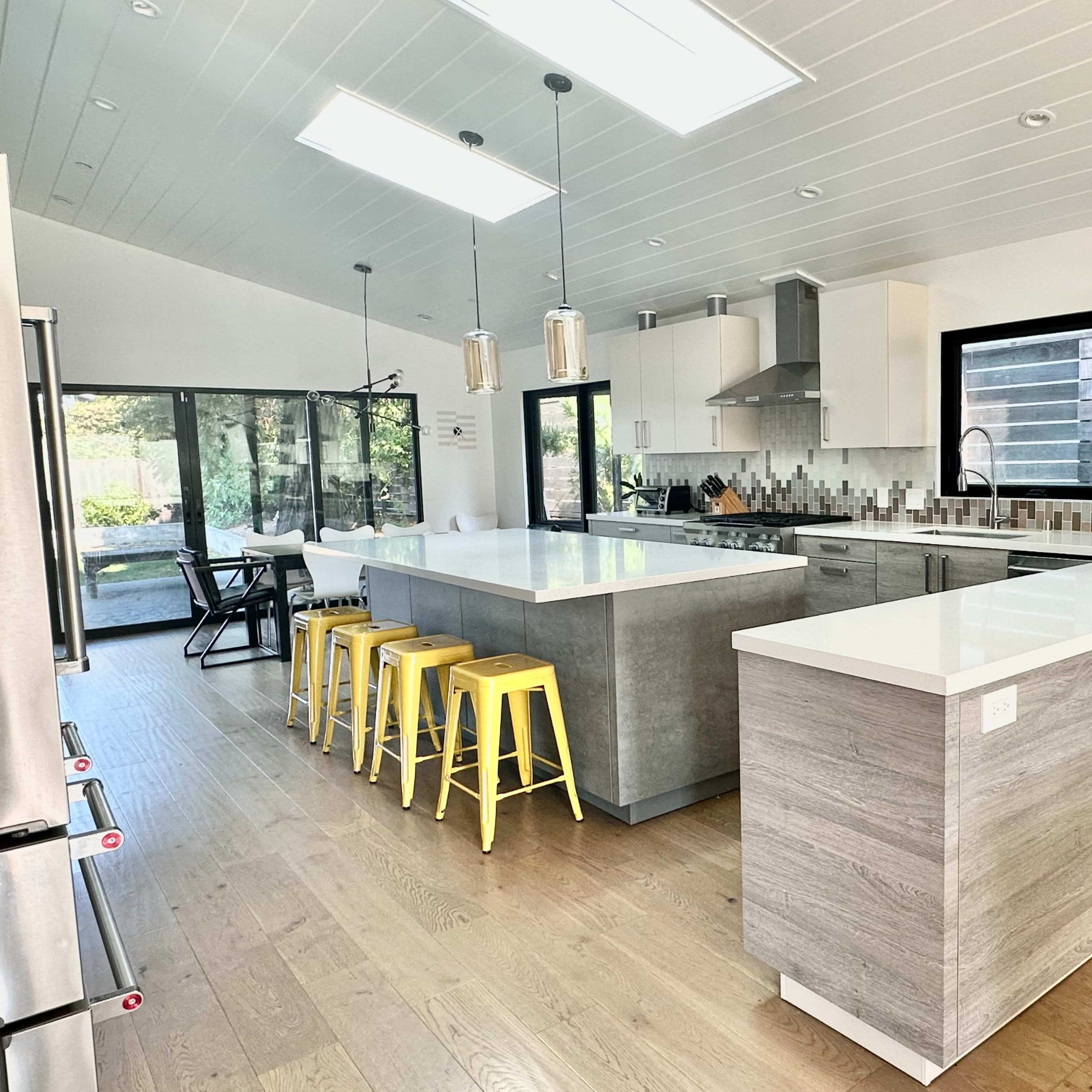 A modern kitchen with a large island, stainless steel appliances, and yellow bar stools.