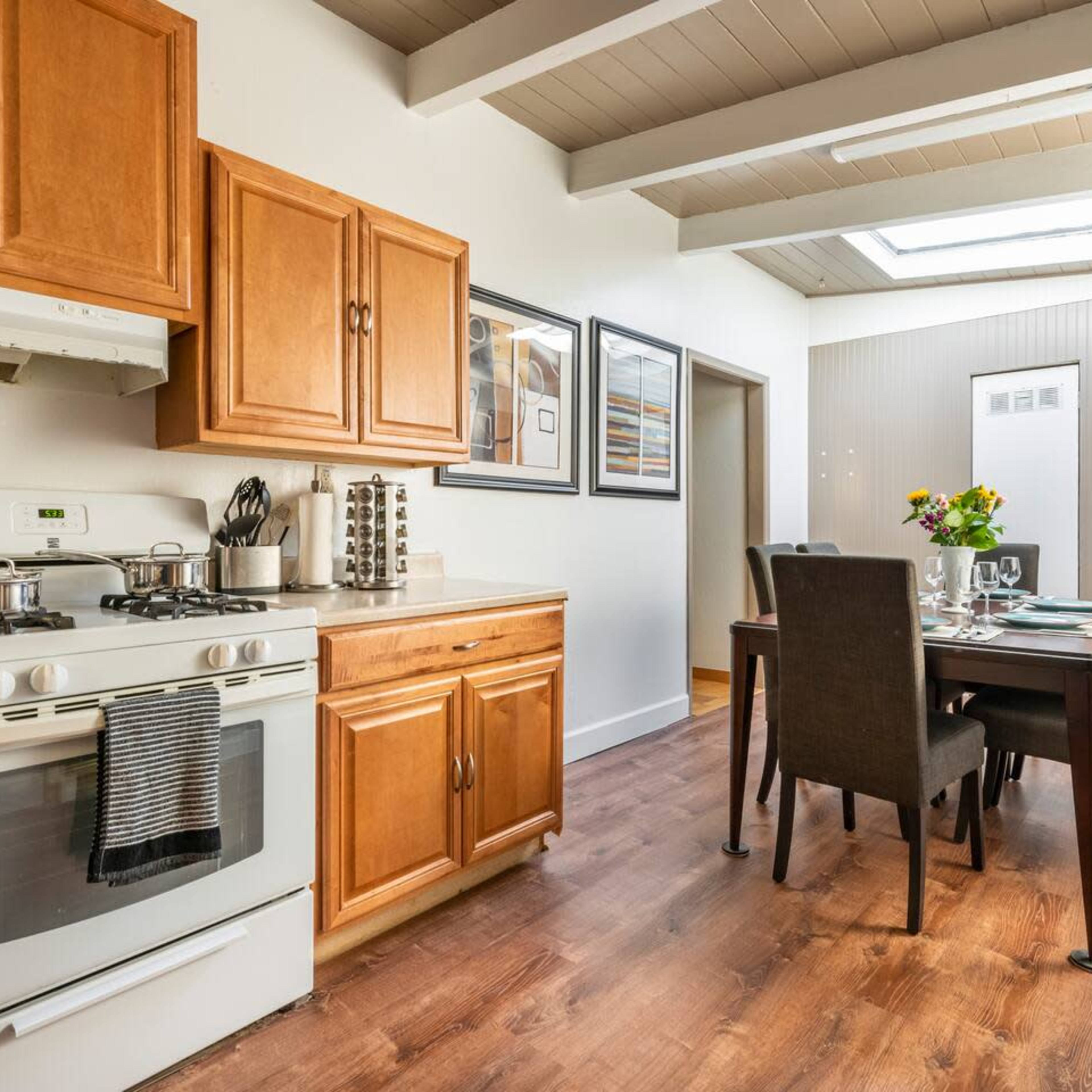 A kitchen and dining area featuring wooden cabinetry, a stove, and a dining table set for a meal.
