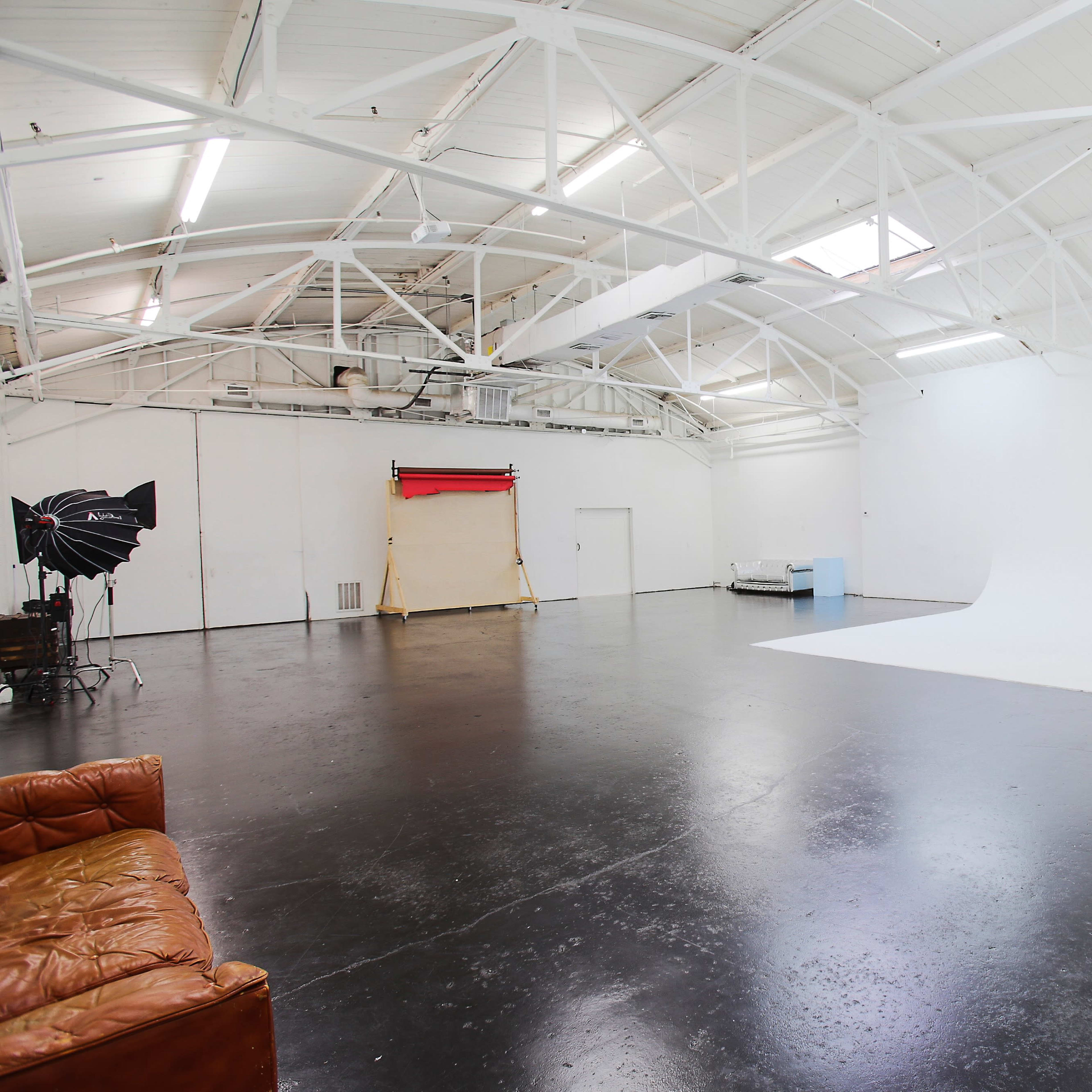 A spacious, well-lit photography studio features a white backdrop, wooden beams, and a dark polished floor.