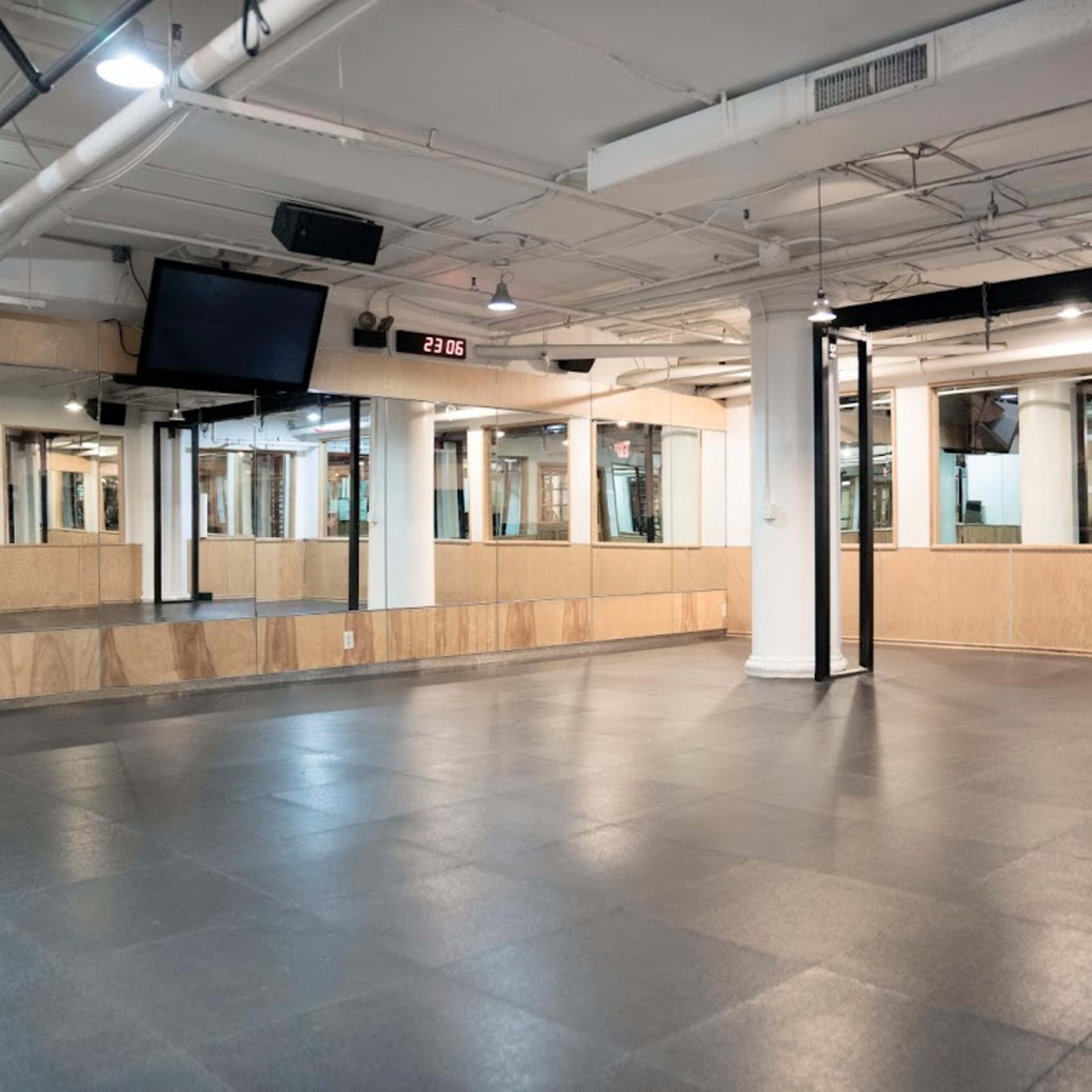 A large, empty indoor studio space with a smooth black floor, white columns, and mirrored walls, illuminated by overhead lighting.