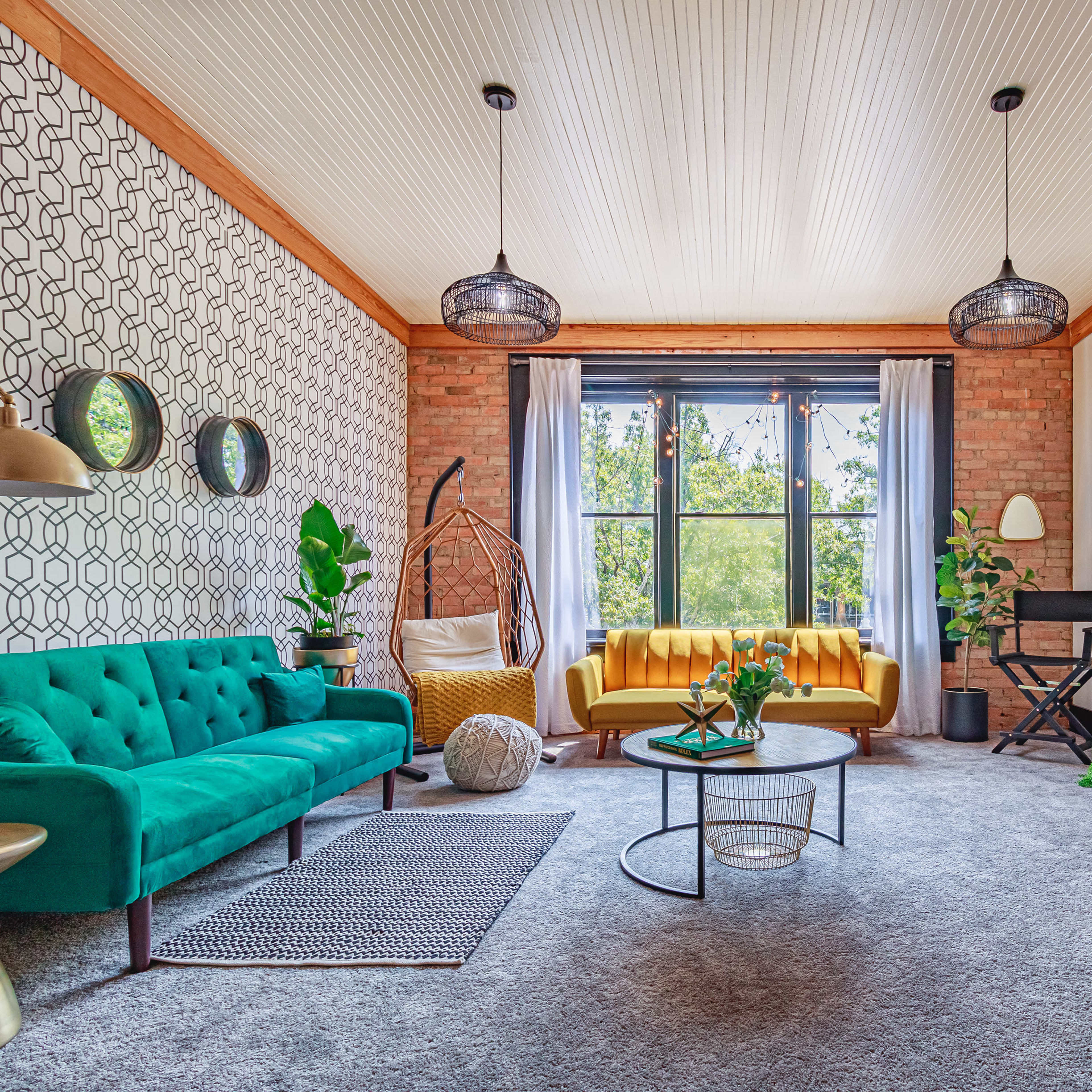A stylish living room with a teal sofa, a yellow couch, a circular coffee table, and a mix of greenery and decorative elements.