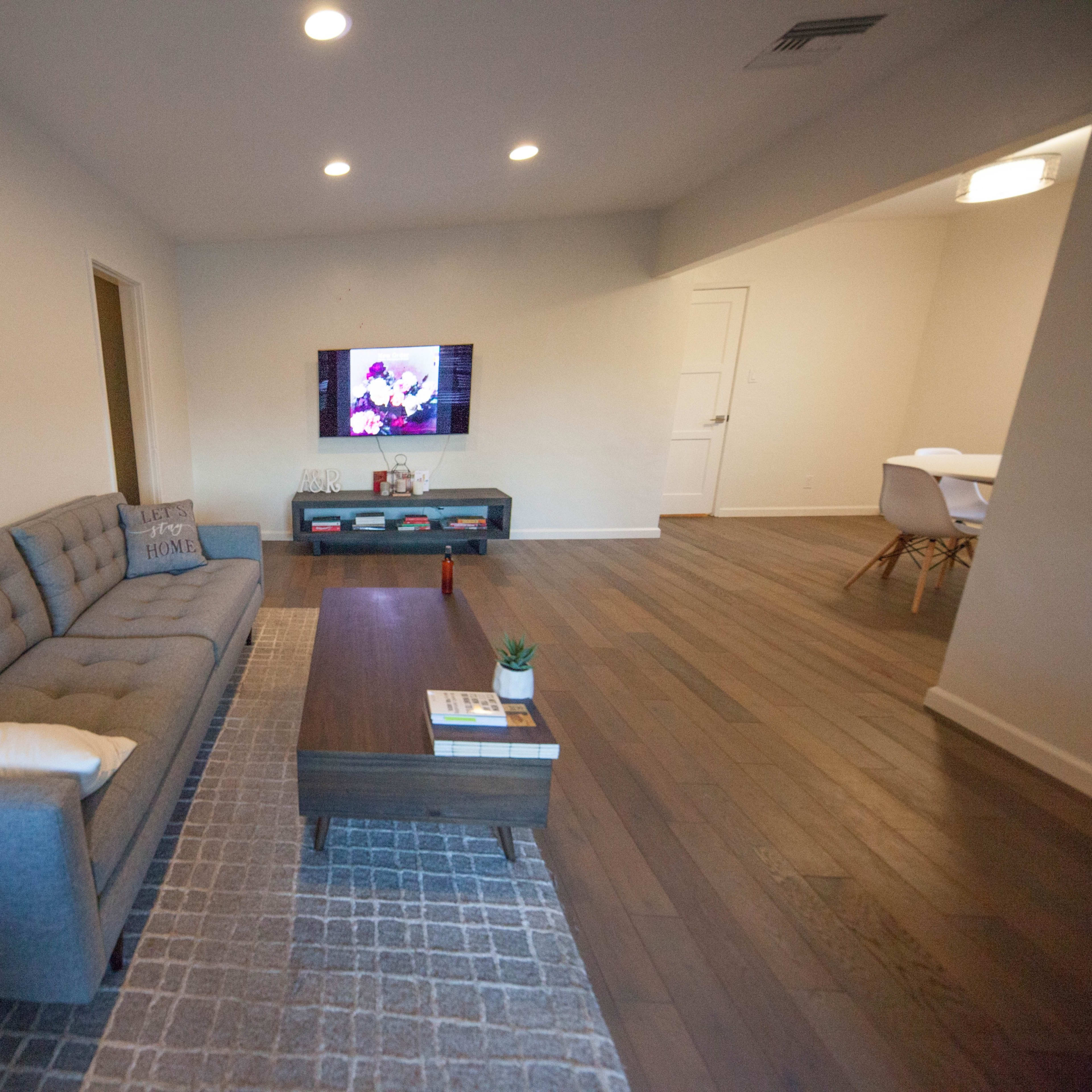 A living room with a gray sofa, a coffee table, a TV mounted on the wall, and hardwood flooring.