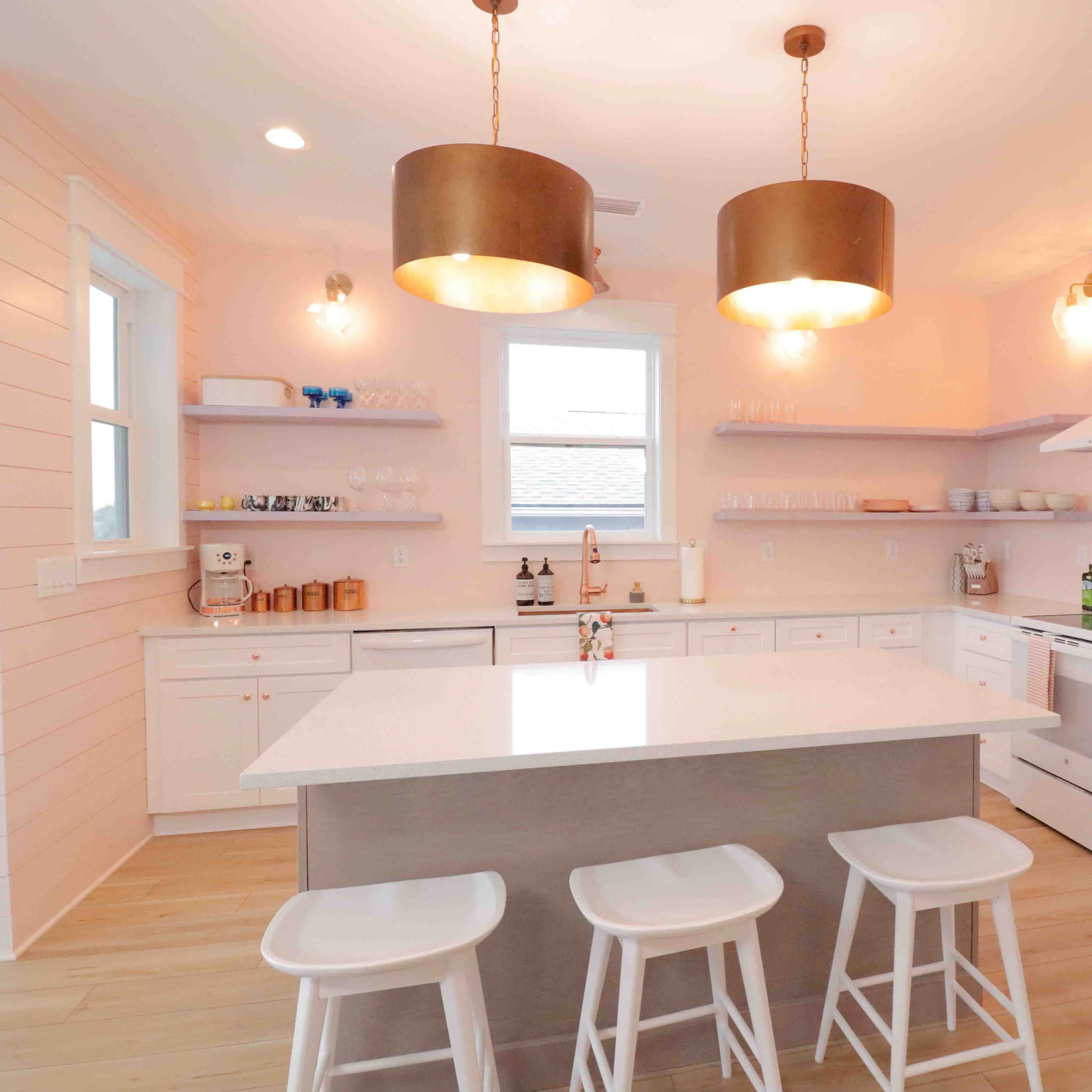 A modern kitchen with white cabinetry, a central island with seating, and pendant lights above.