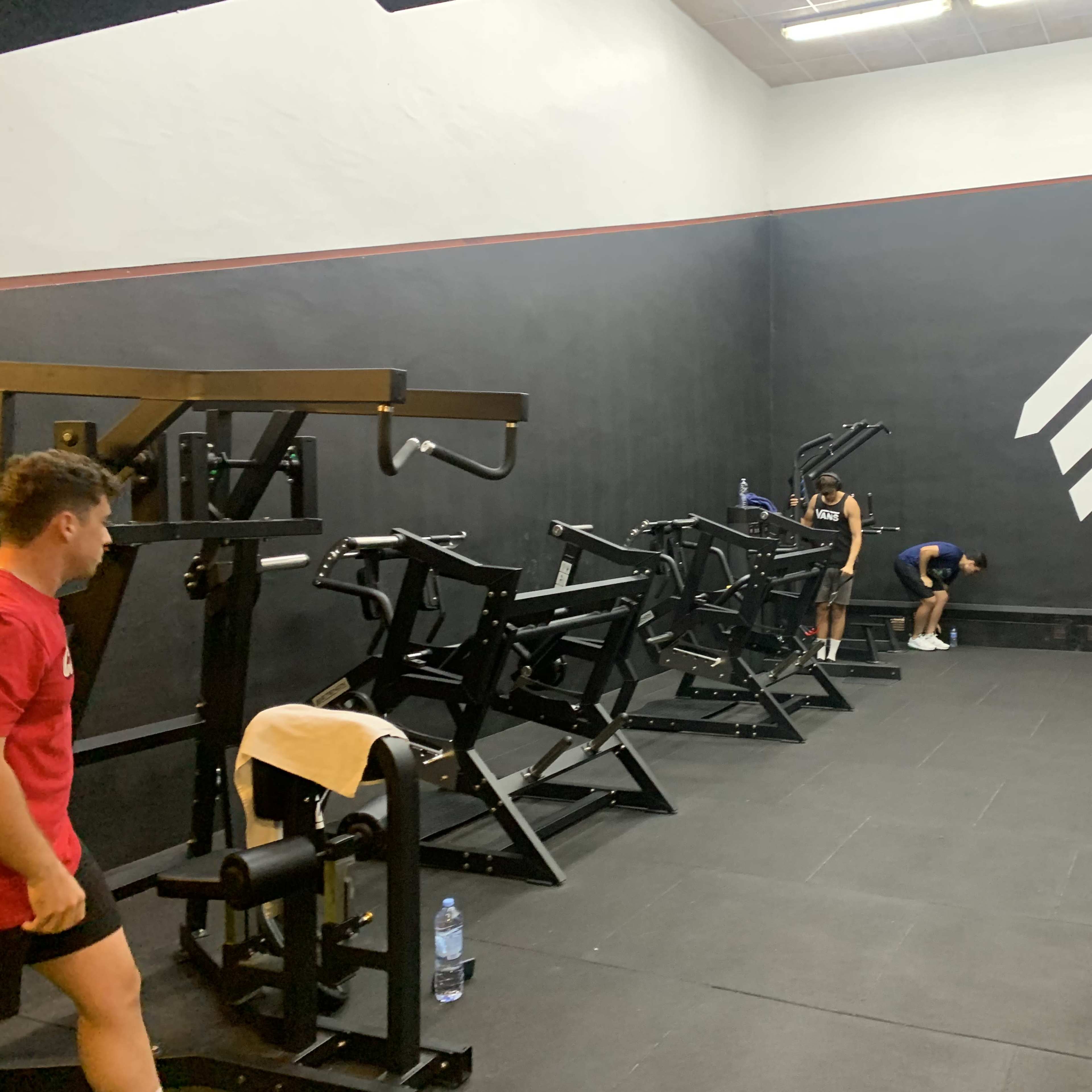 A dimly lit gym with workout equipment on one side and three individuals engaged in exercises.