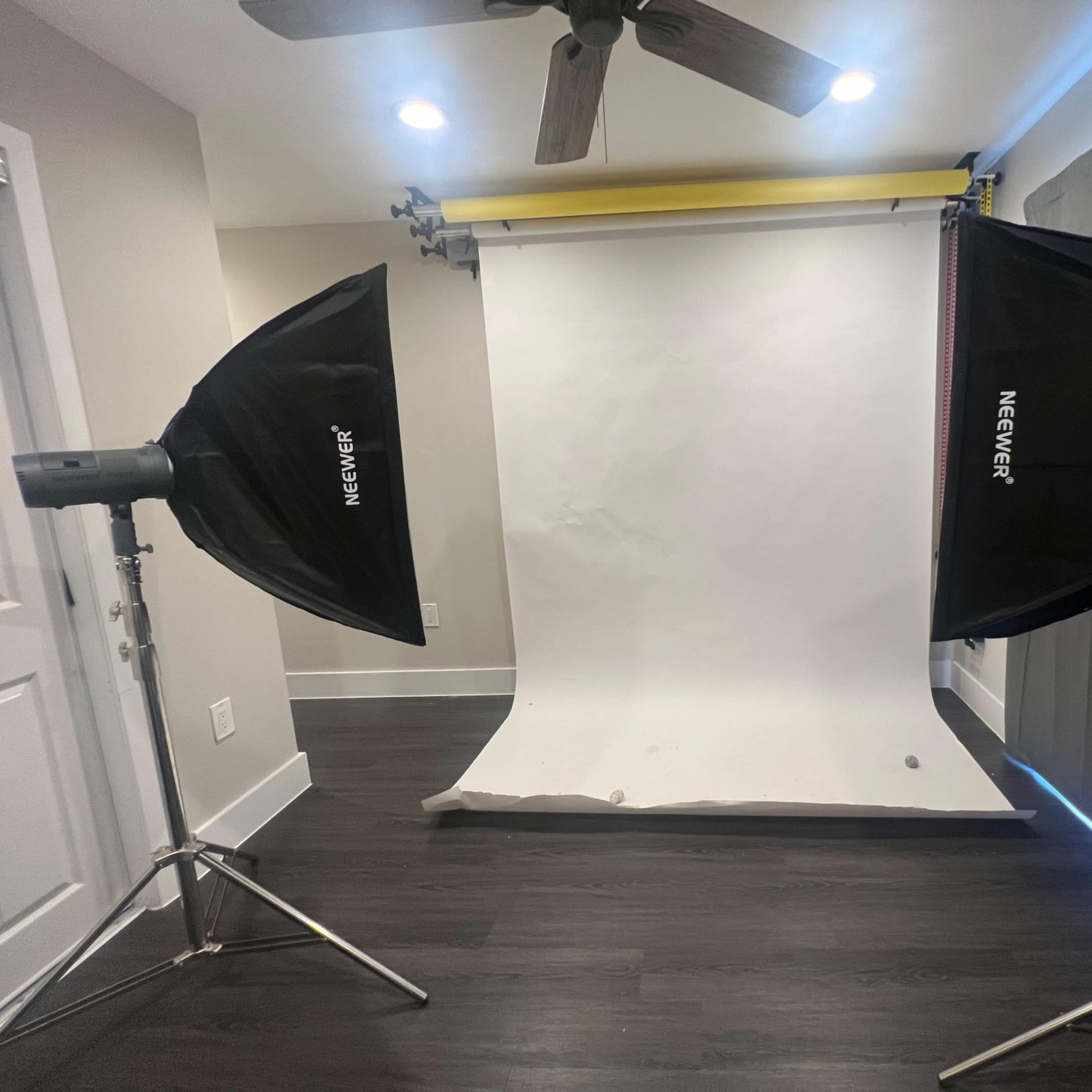 A photography studio setup with two softbox lights positioned on either side of a white backdrop.