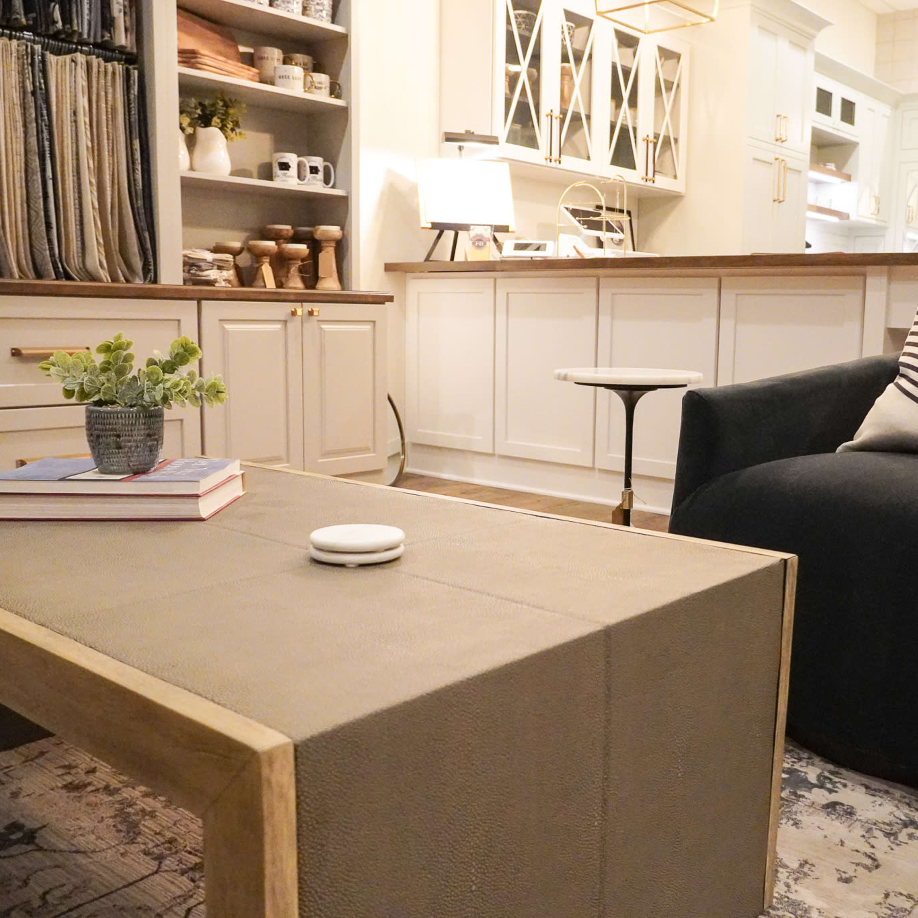 A modern living area features a black armchair, a coffee table with a textured surface, and a backdrop of neatly arranged kitchen cabinetry.