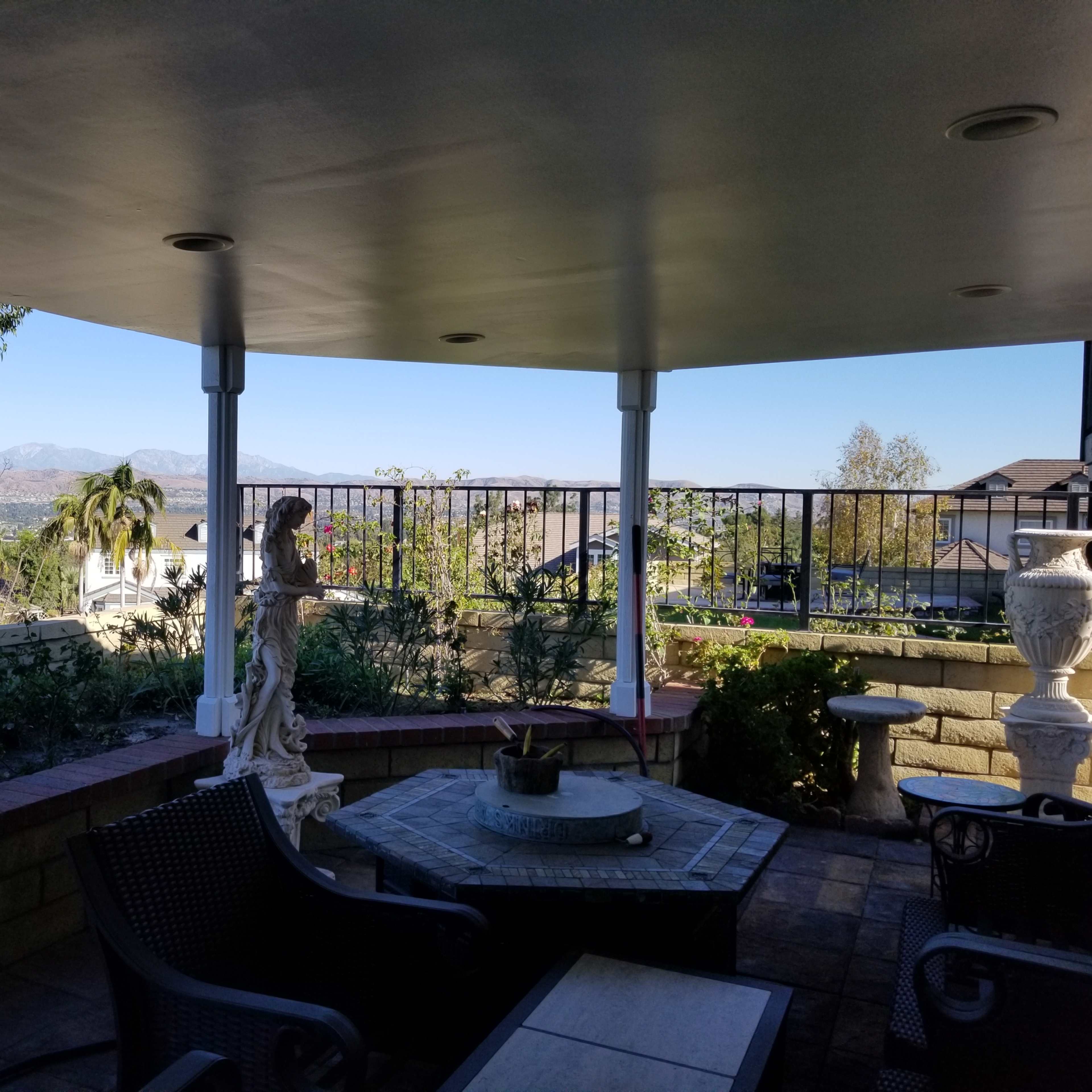 A covered patio area with outdoor furniture, overlooking a landscaped yard and distant mountains.