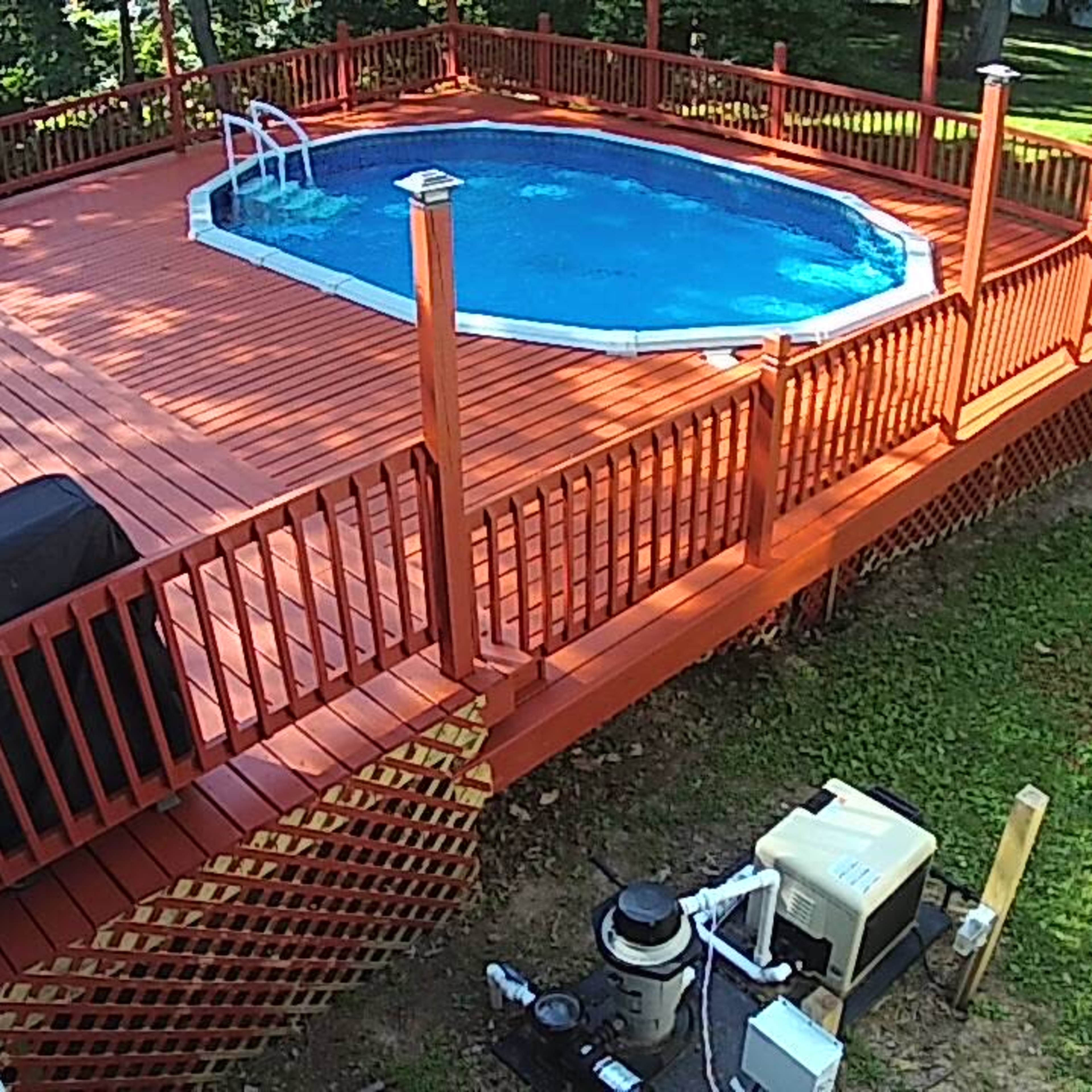 A backyard scene with a circular pool surrounded by a wooden deck, chairs, and a pool pump unit nearby.