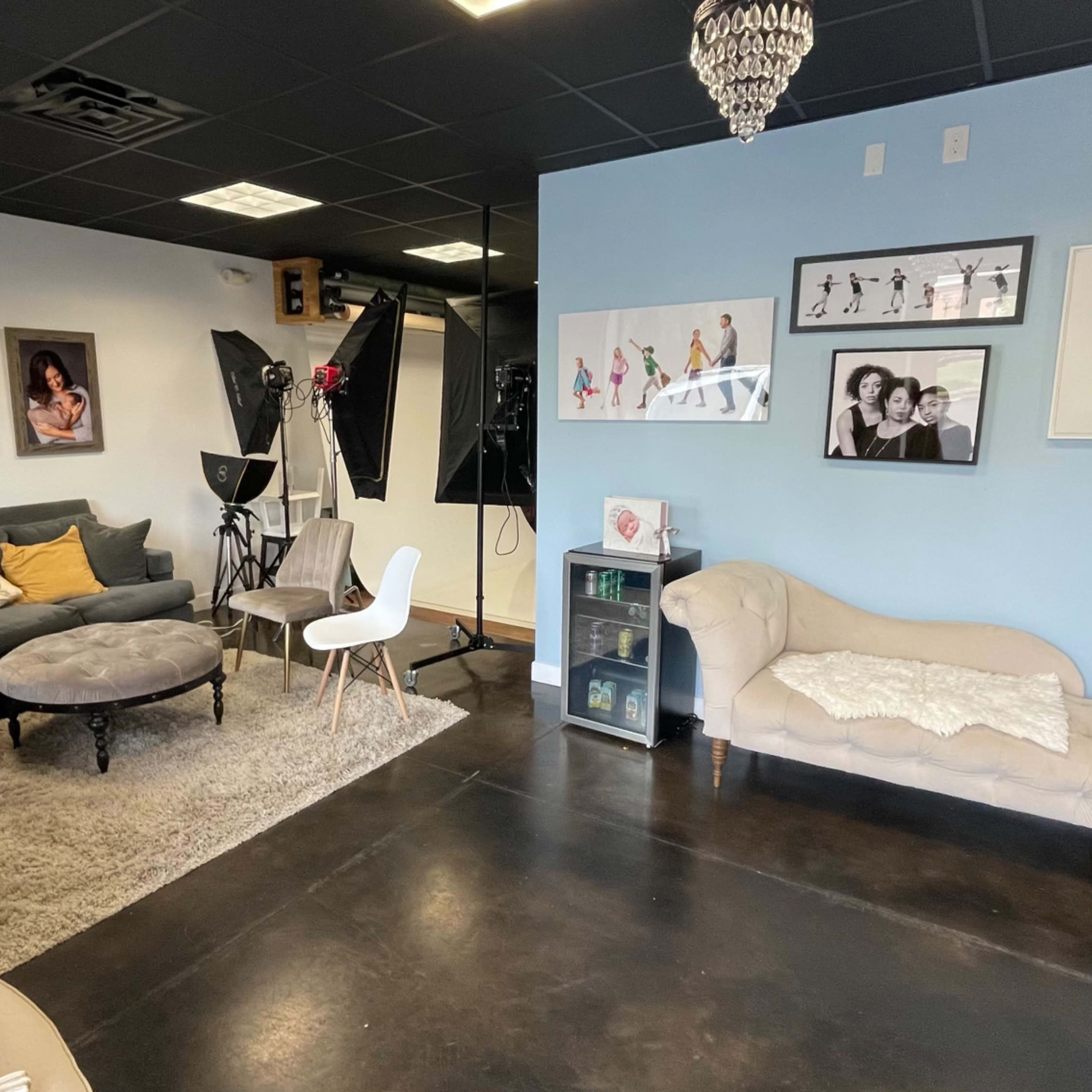 A studio space with a seating area featuring a gray couch, a round coffee table, and various framed photographs on the walls.