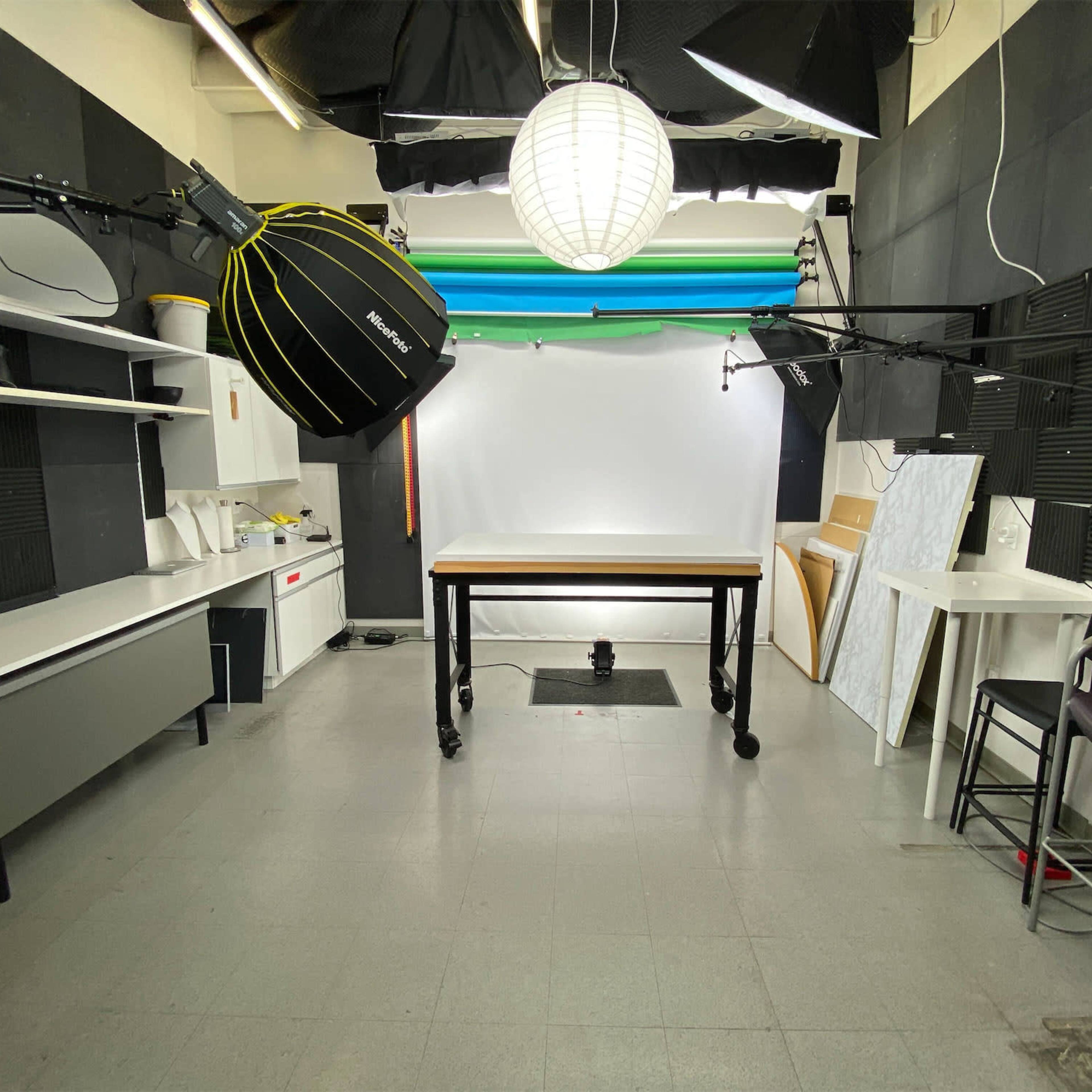 A photography studio with a large table in the center, surrounded by lighting equipment and a backdrop on the wall.