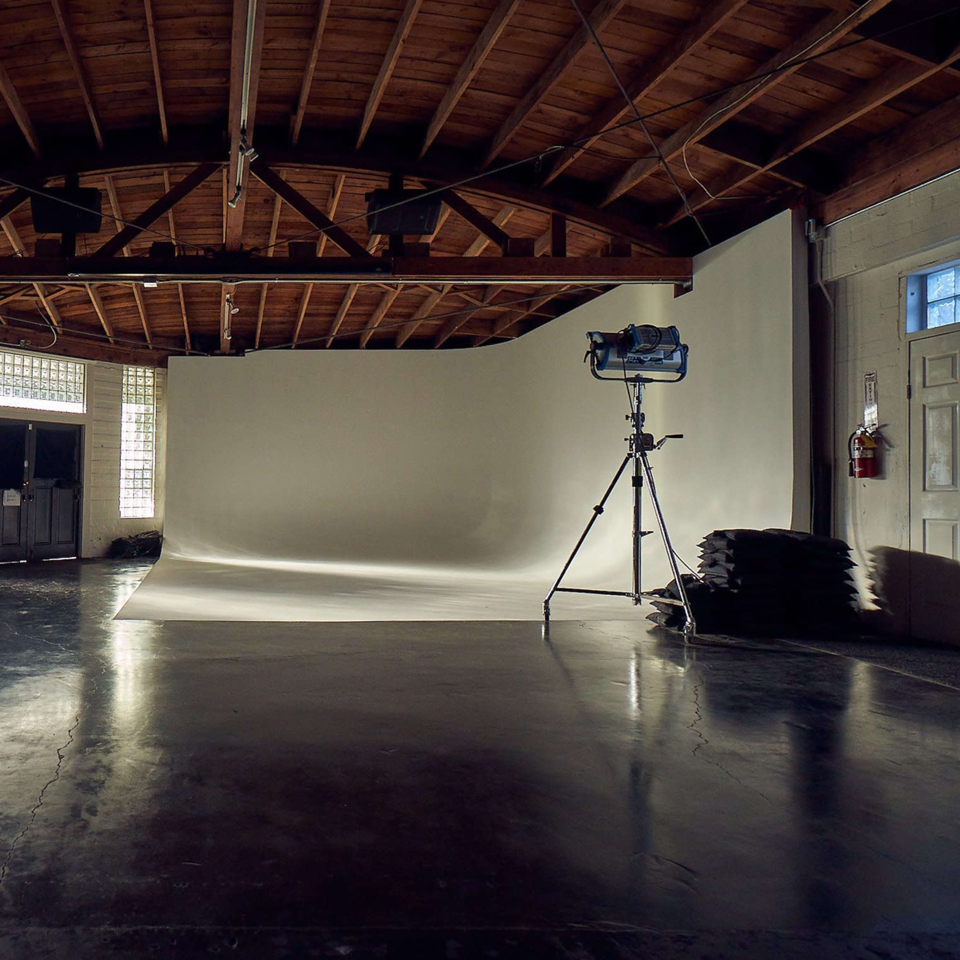A photography studio features a seamless backdrop, a lighting setup on a tripod, and large windows allowing natural light.
