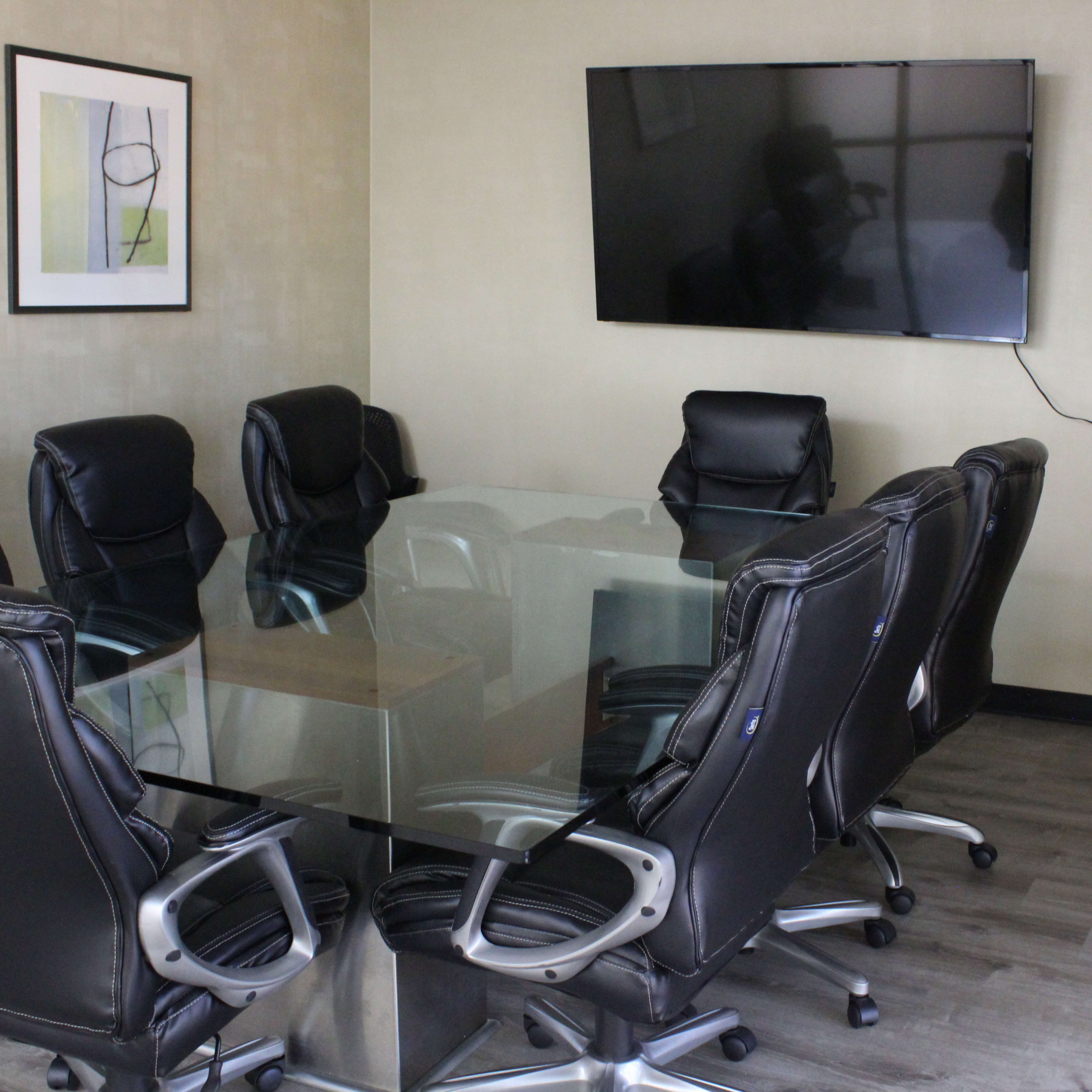 A conference room with a glass table surrounded by several black ergonomic chairs and a mounted television on the wall.