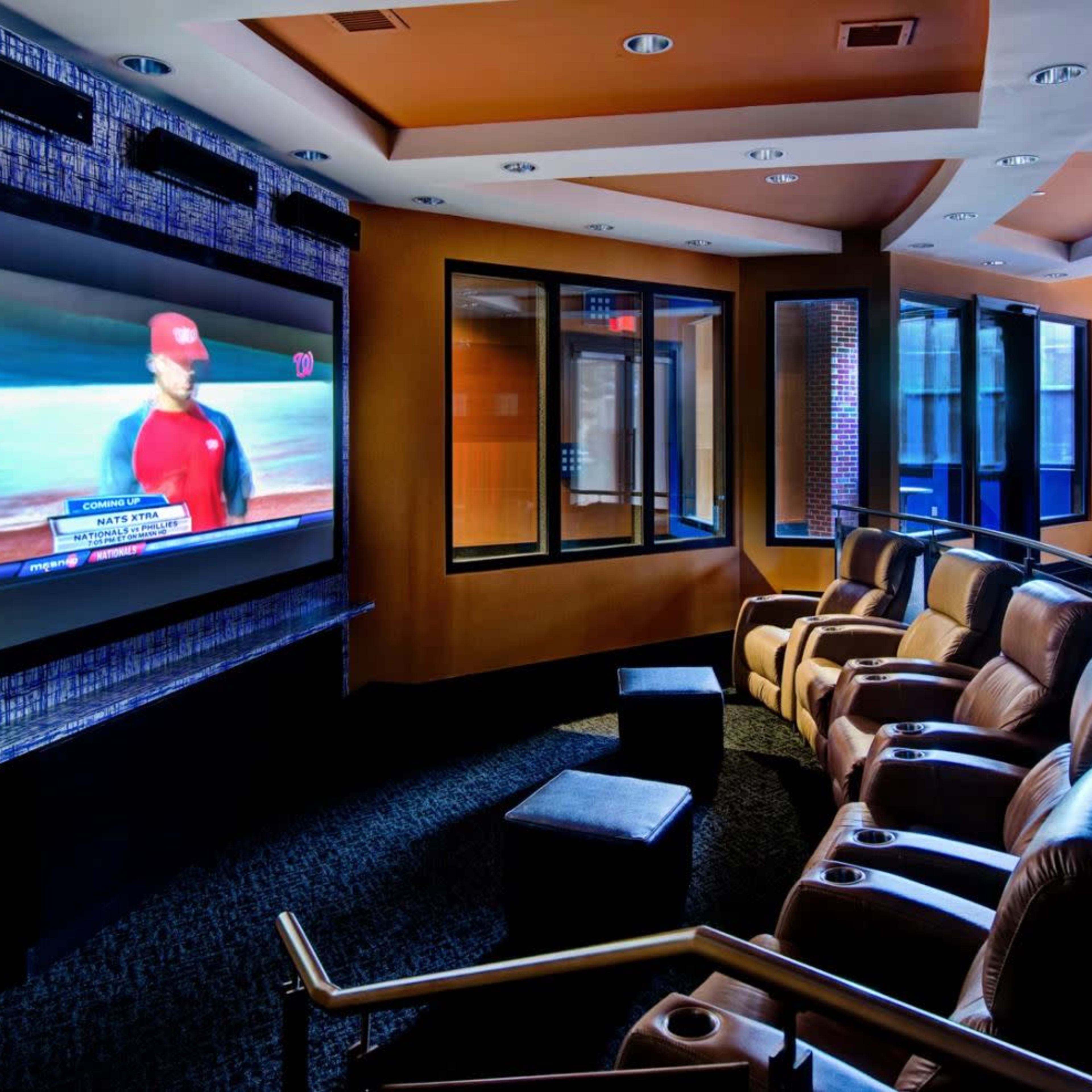 A home theater features leather reclining seats facing a large television mounted on the wall.