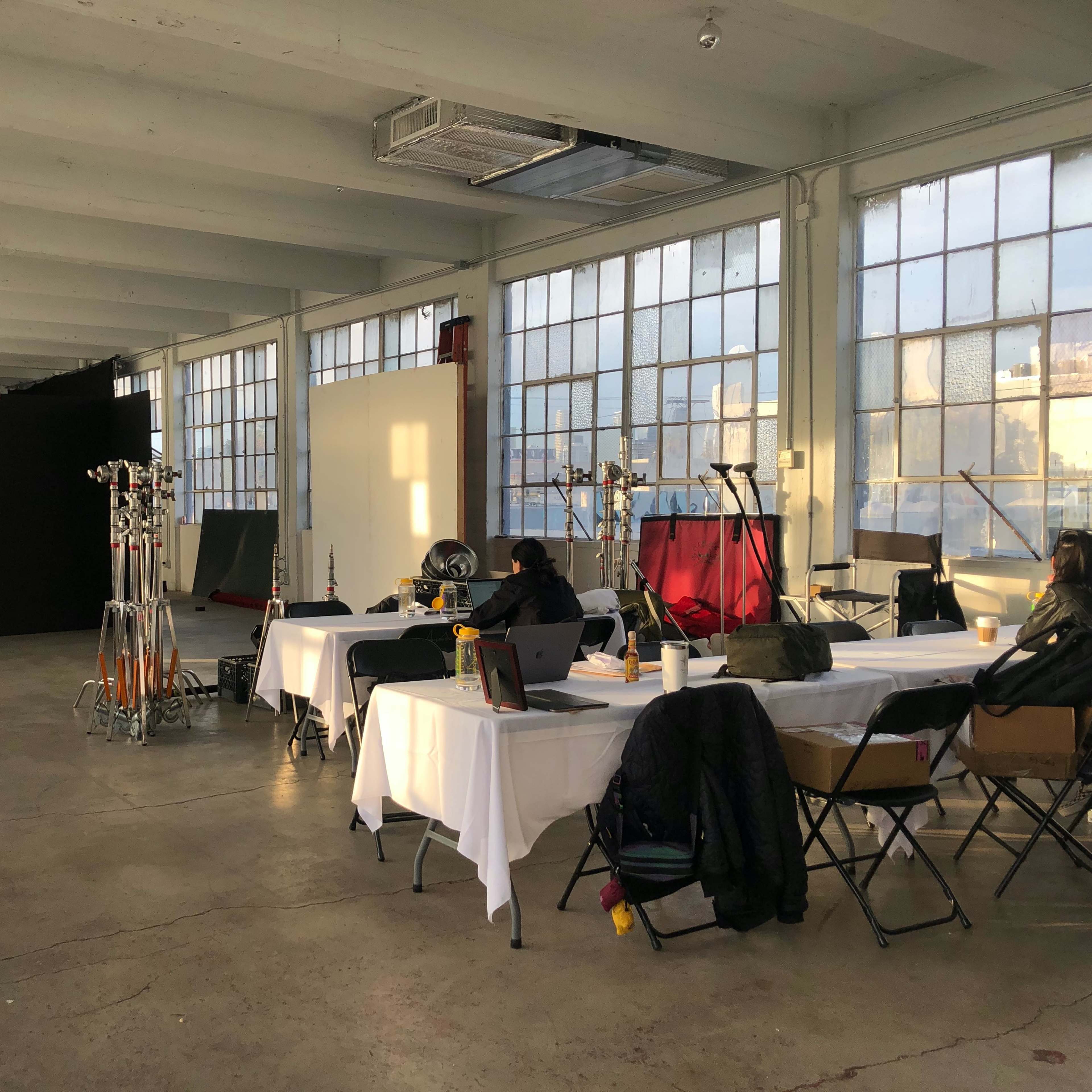 A spacious studio with large windows, tables set for a shoot, and equipment lined along the walls.