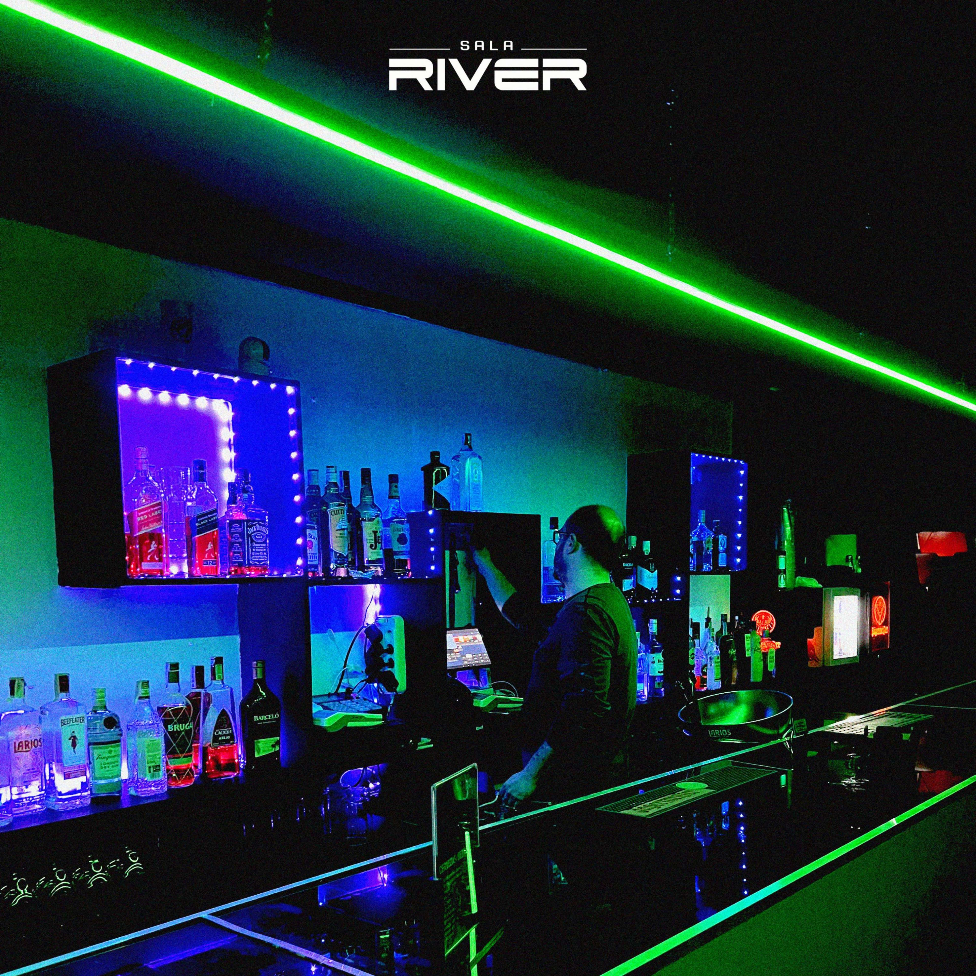 A bartender prepares drinks behind a sleek bar illuminated by green and blue LED lights, with various bottles displayed on shelves.