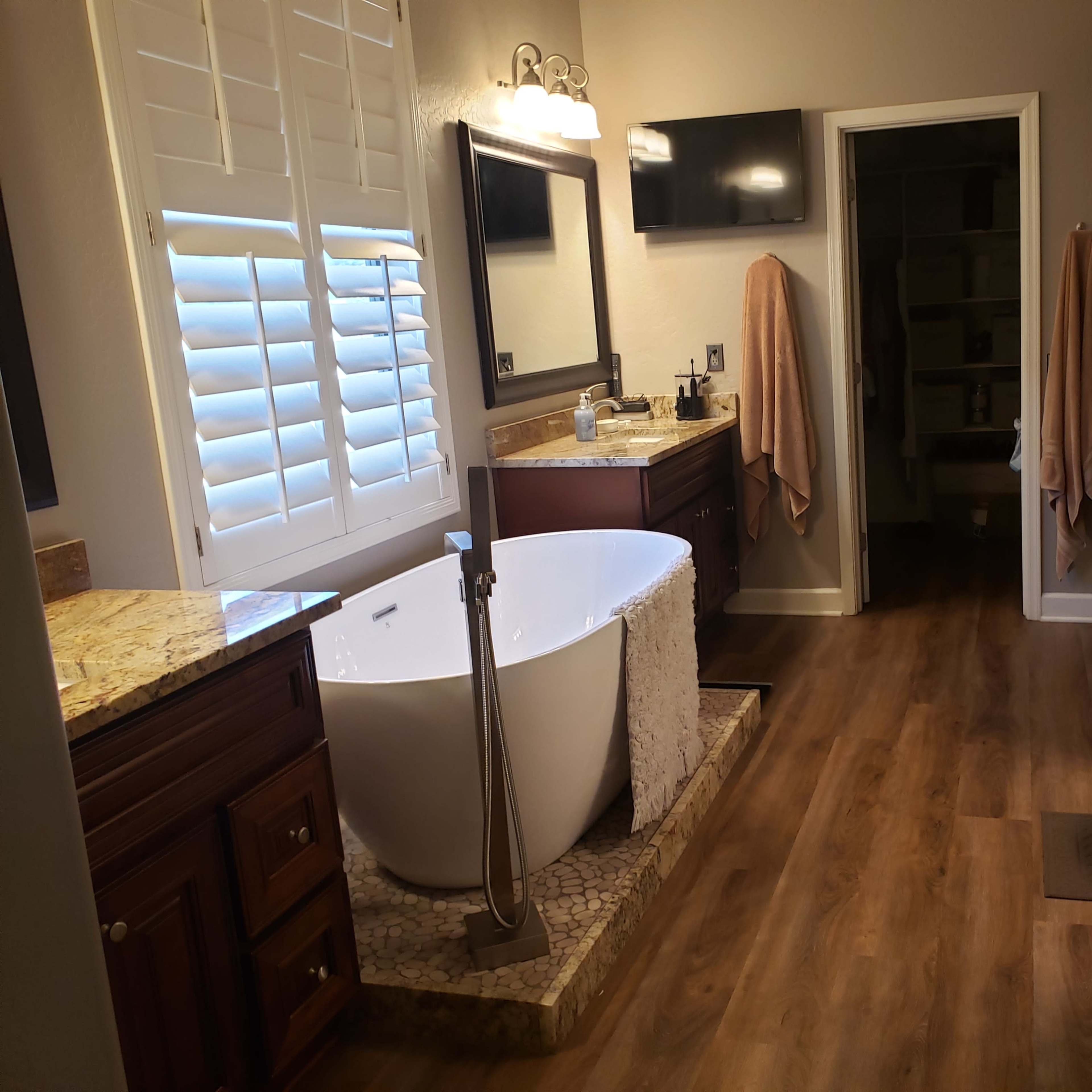 A modern bathroom features a freestanding tub, dual sinks with wooden cabinetry, and a well-lit space with a door leading to a closet.