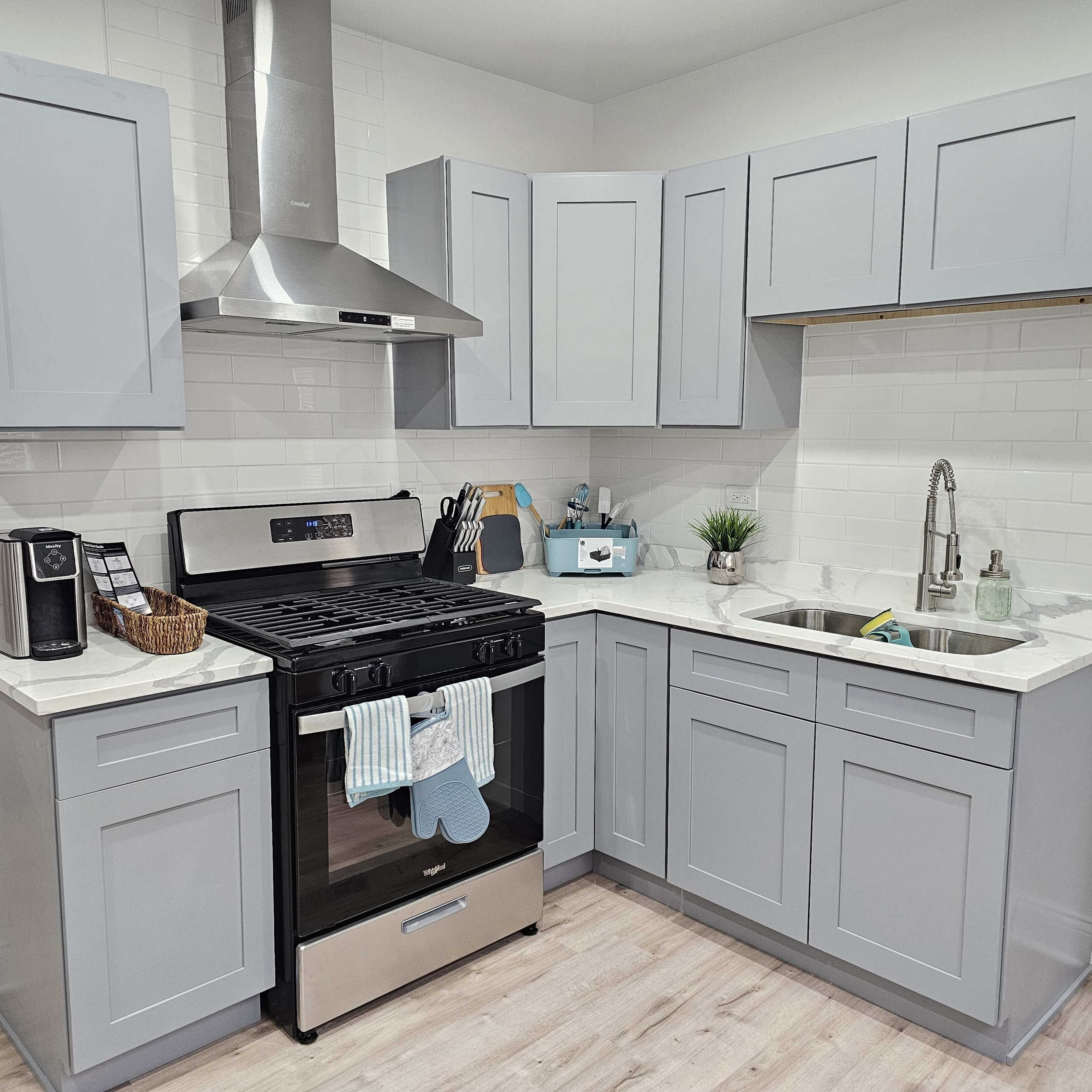 A modern kitchen with gray cabinetry, a stainless steel stove, and a double sink with a minimalist decor.