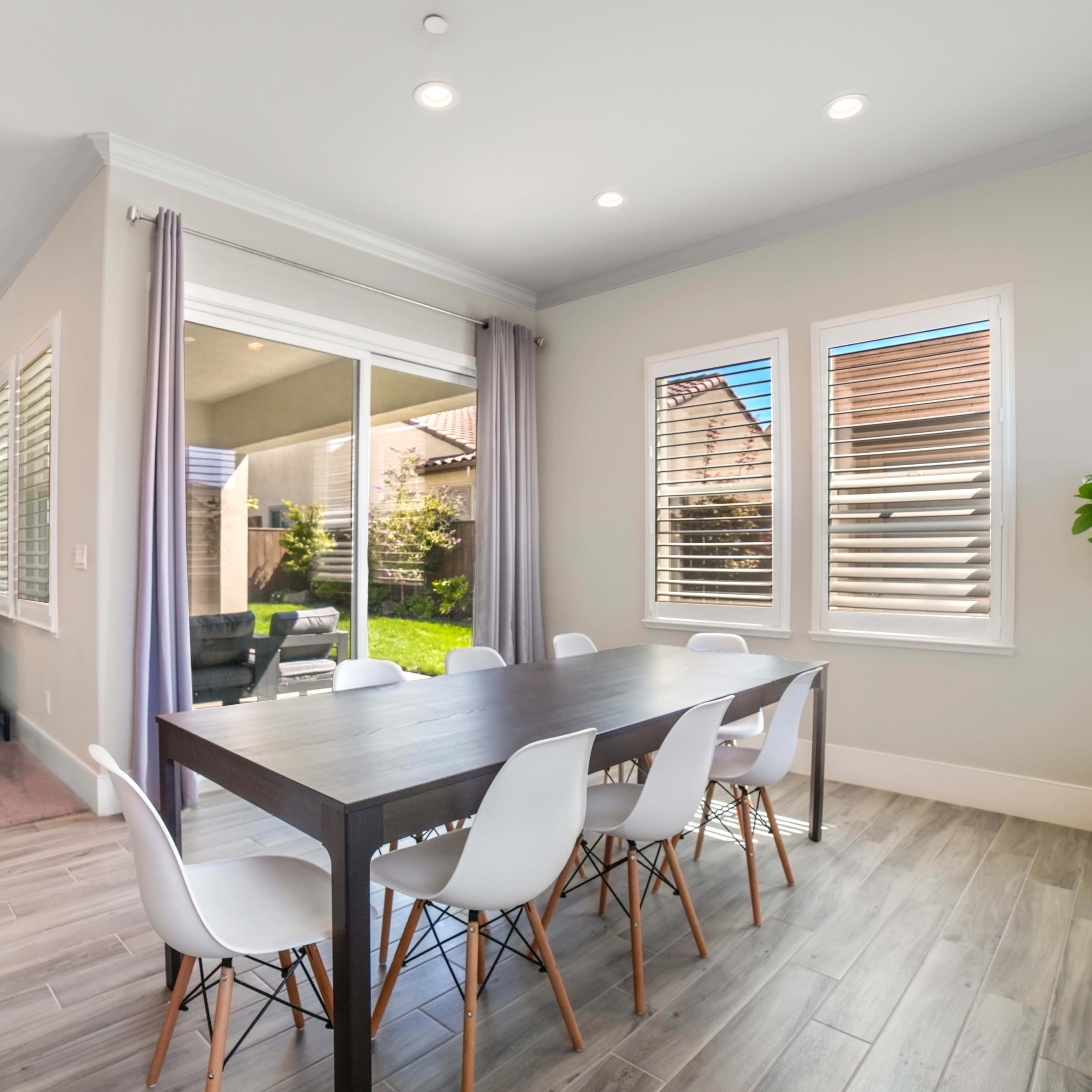 A modern dining area with a wooden table surrounded by white chairs, illuminated by natural light from nearby windows.