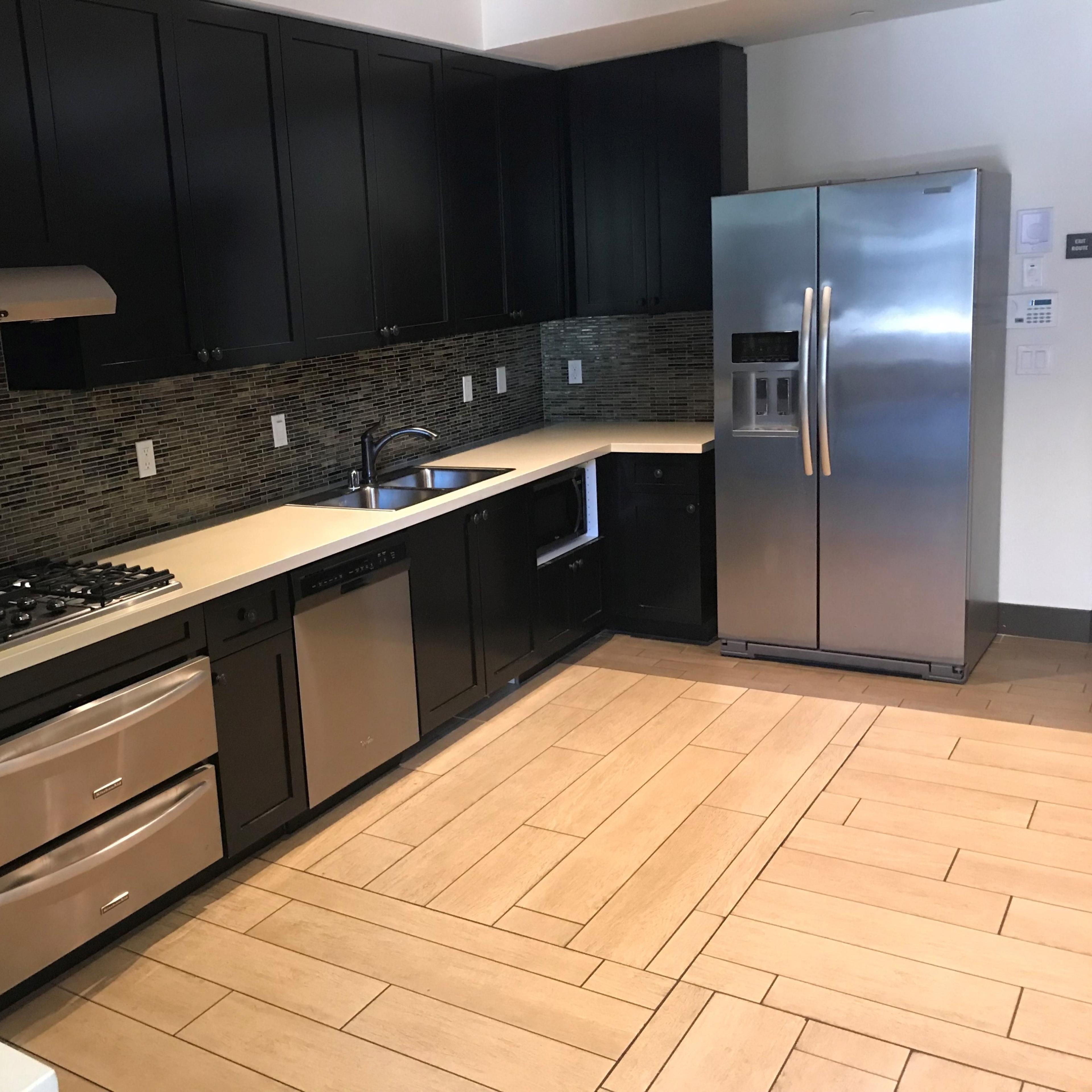 A modern kitchen with dark cabinetry, a stainless steel refrigerator, and a countertop with a gas stove and sink.