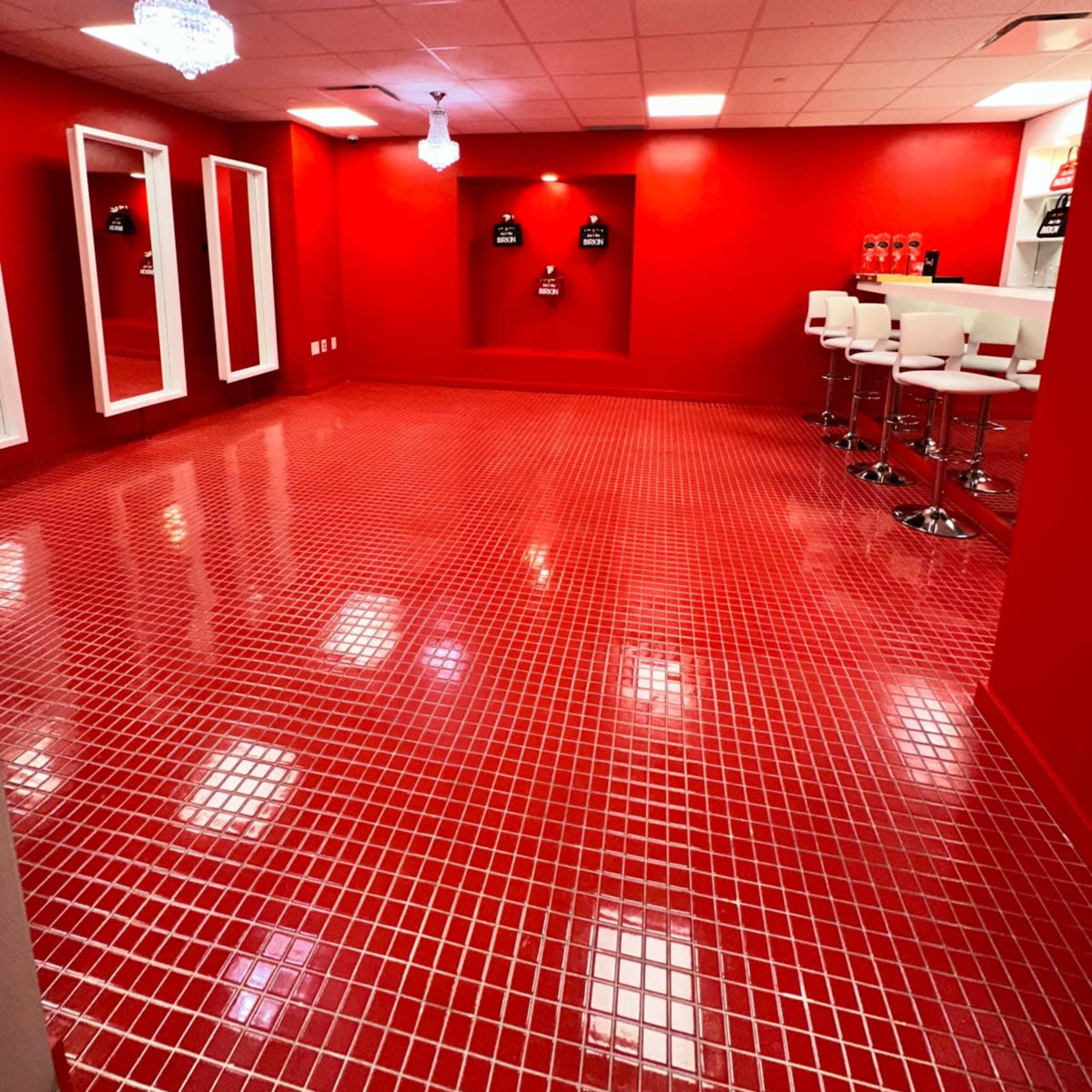 A brightly lit room with red tiled flooring, red walls, and modern white bar stools.