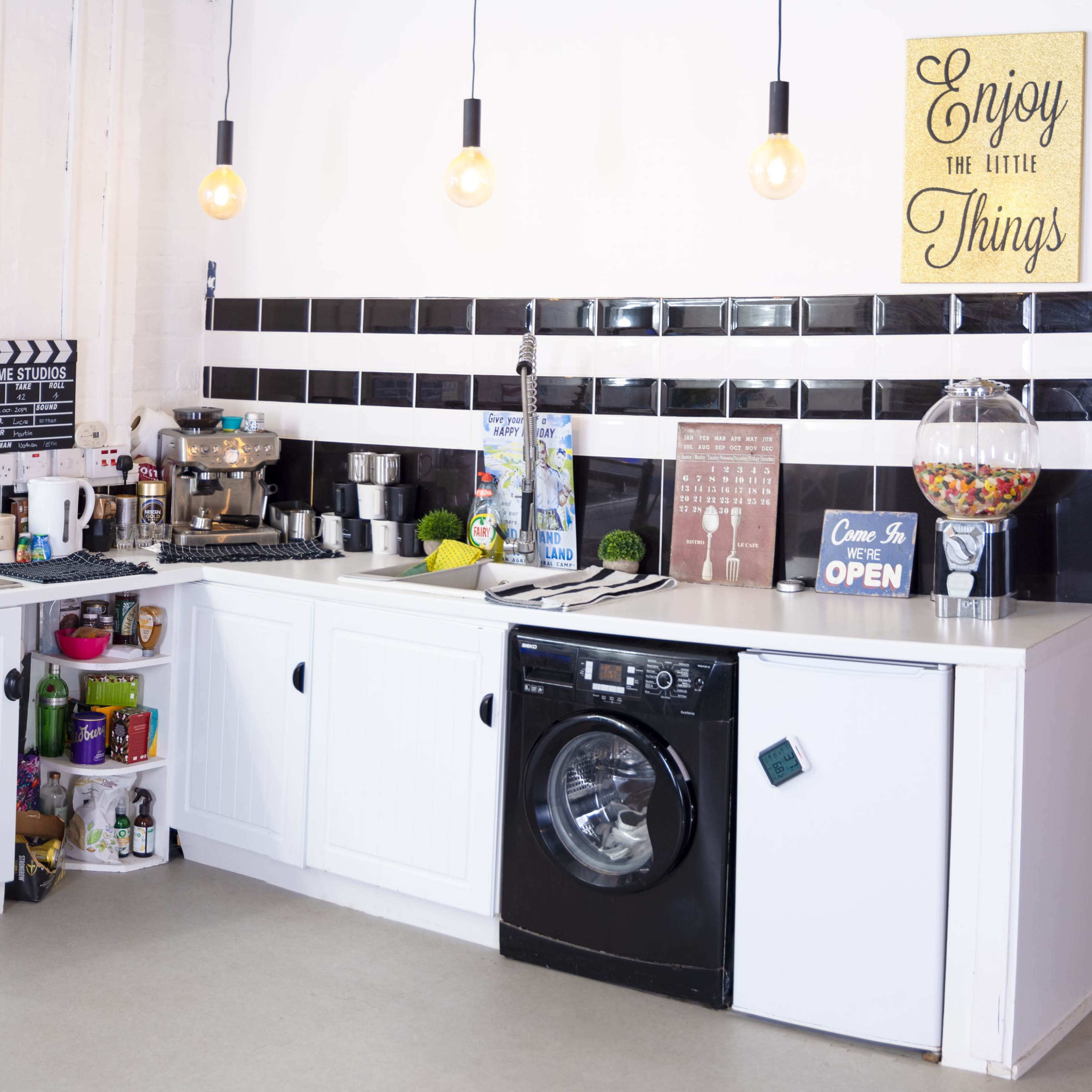 A modern kitchen with a white color scheme, featuring a black-tiled backsplash, a washing machine, and various kitchen appliances.