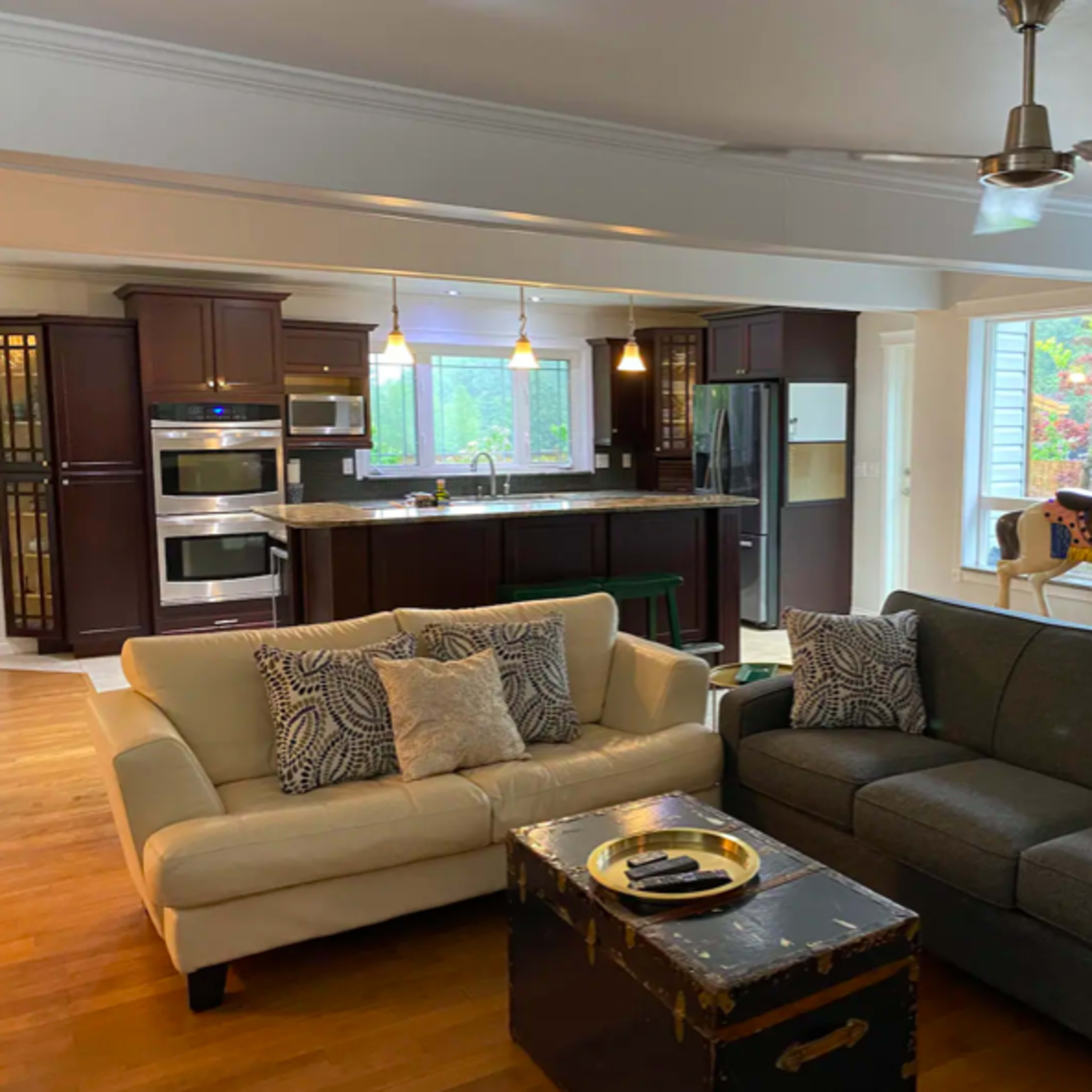 A living room with two sofas, a coffee table, and a kitchen in the background featuring stainless steel appliances and a horse figurine in the corner.