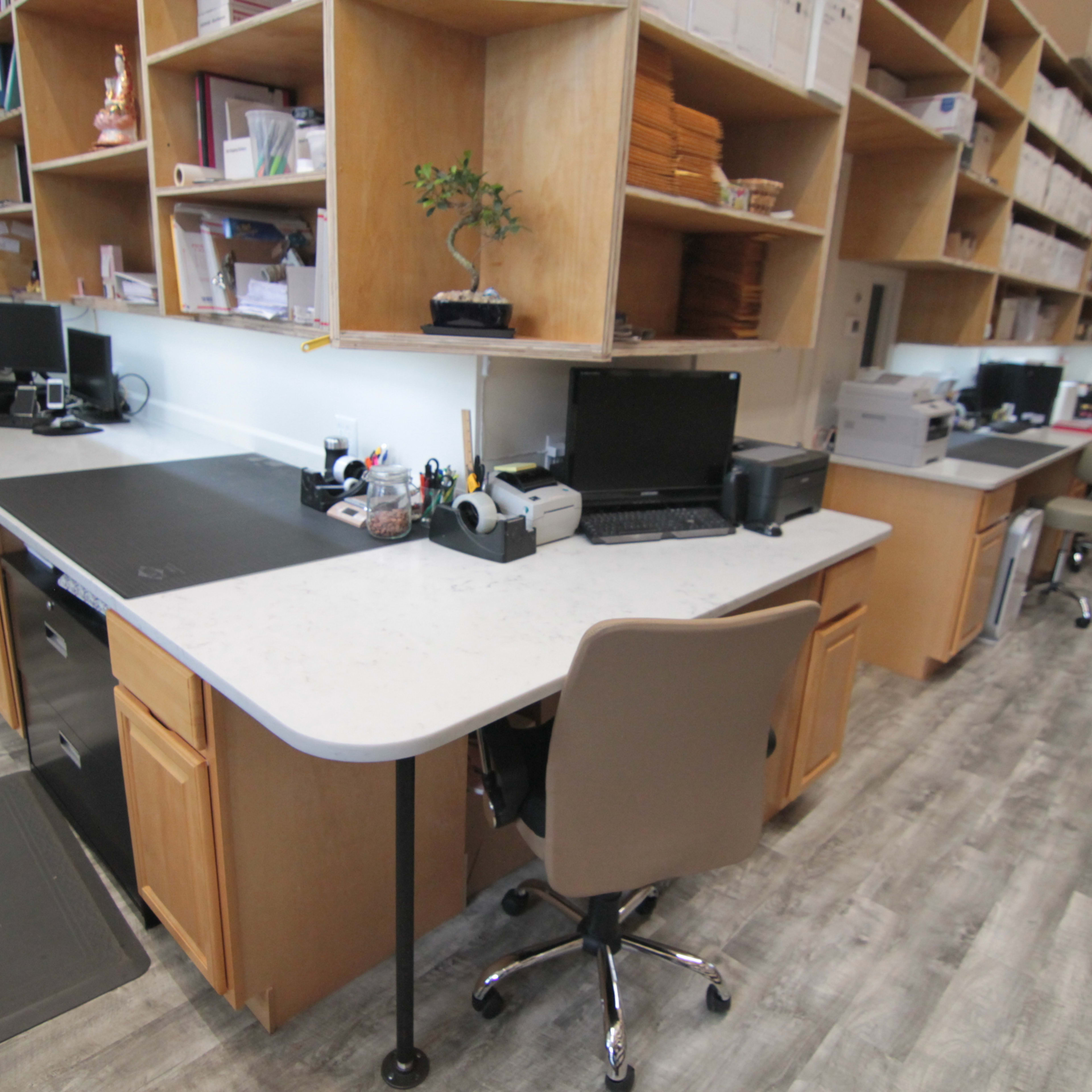 A modern office space with multiple desks equipped with computers and office supplies, surrounded by wooden shelves filled with documents.