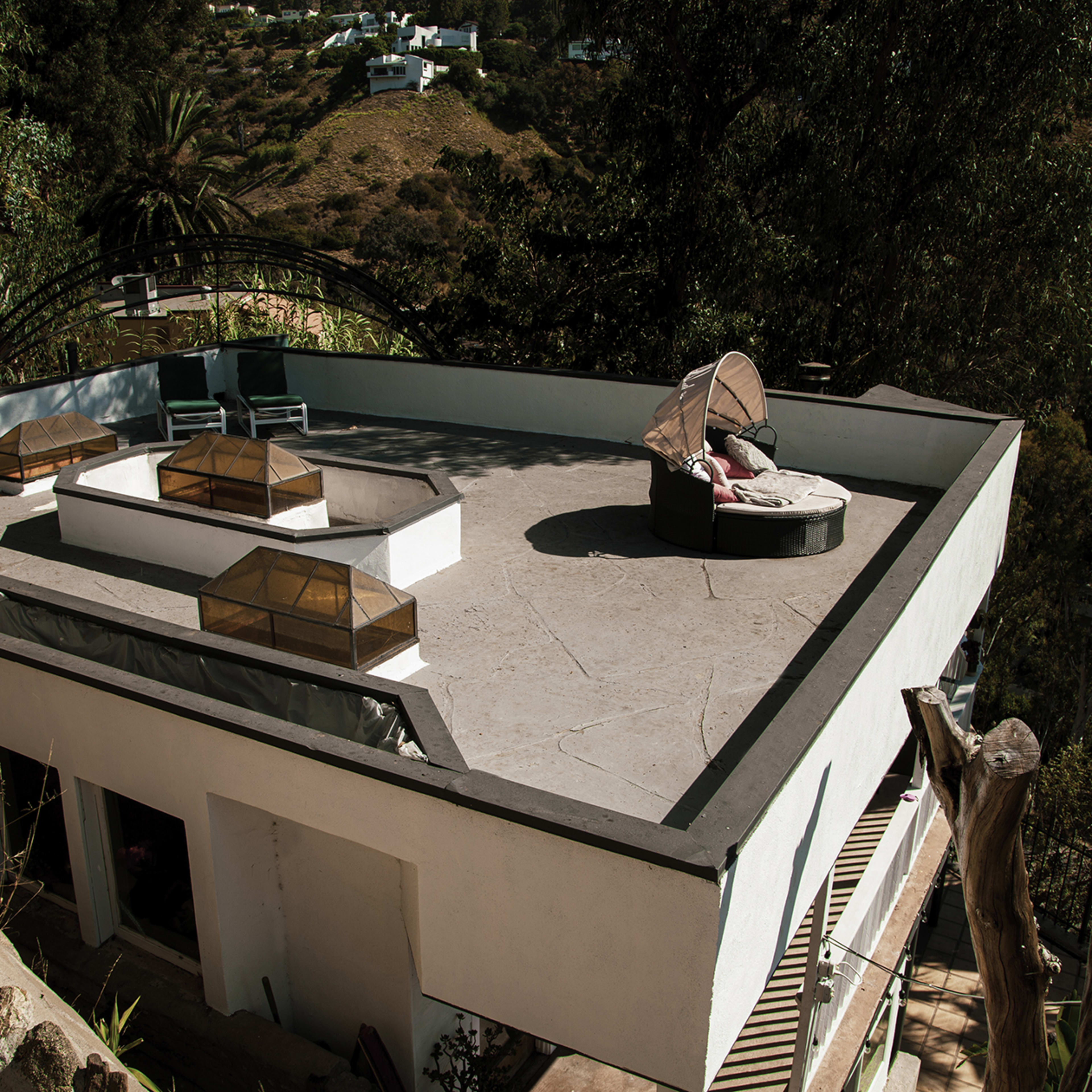 A modern rooftop terrace with lounge furniture and glass skylights surrounded by greenery and hills.