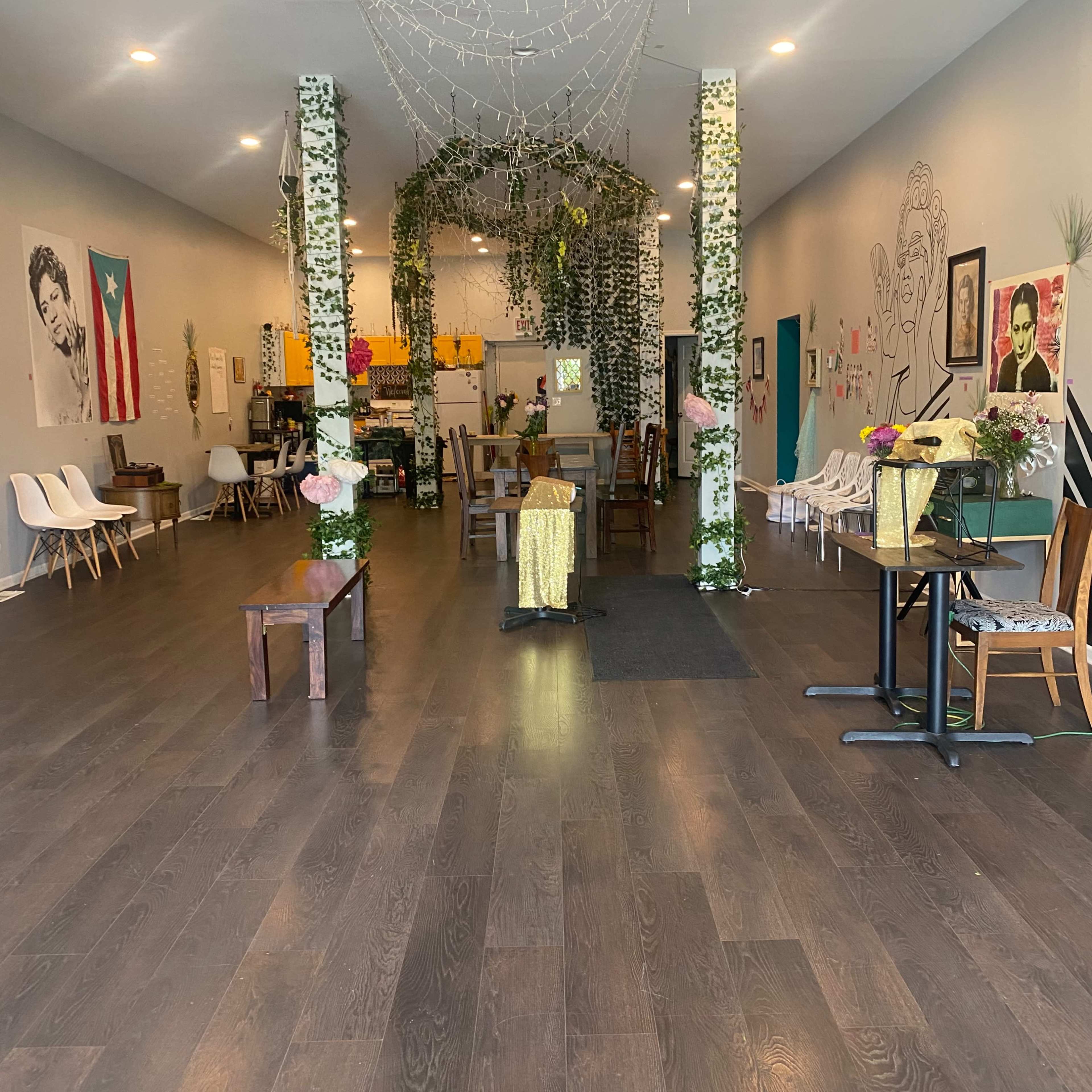 A spacious, decorated interior of a cafe featuring plants, artwork on the walls, and a mix of seating arrangements.