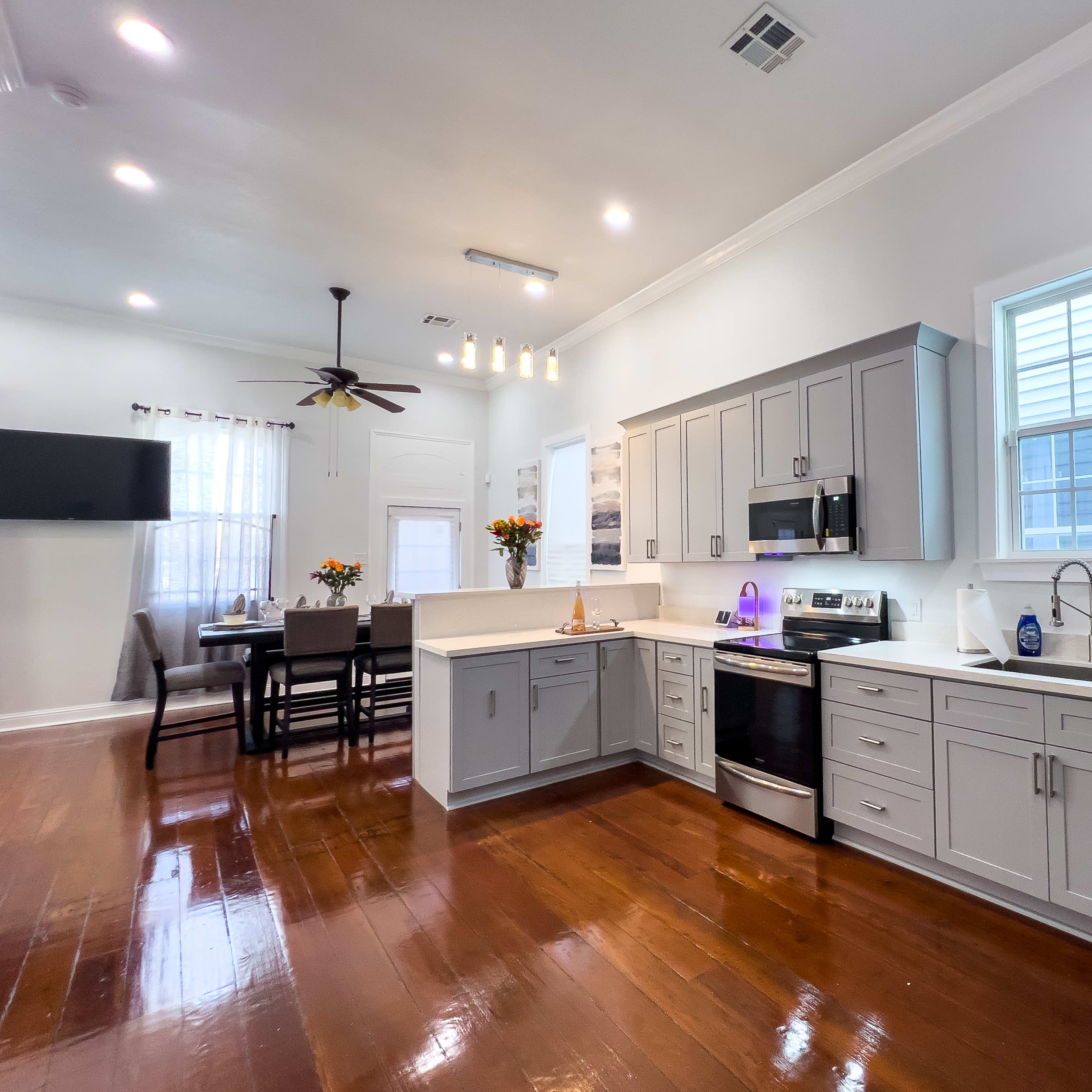 A modern kitchen with gray cabinets, stainless steel appliances, and a dining area featuring a table and chairs in a well-lit space.