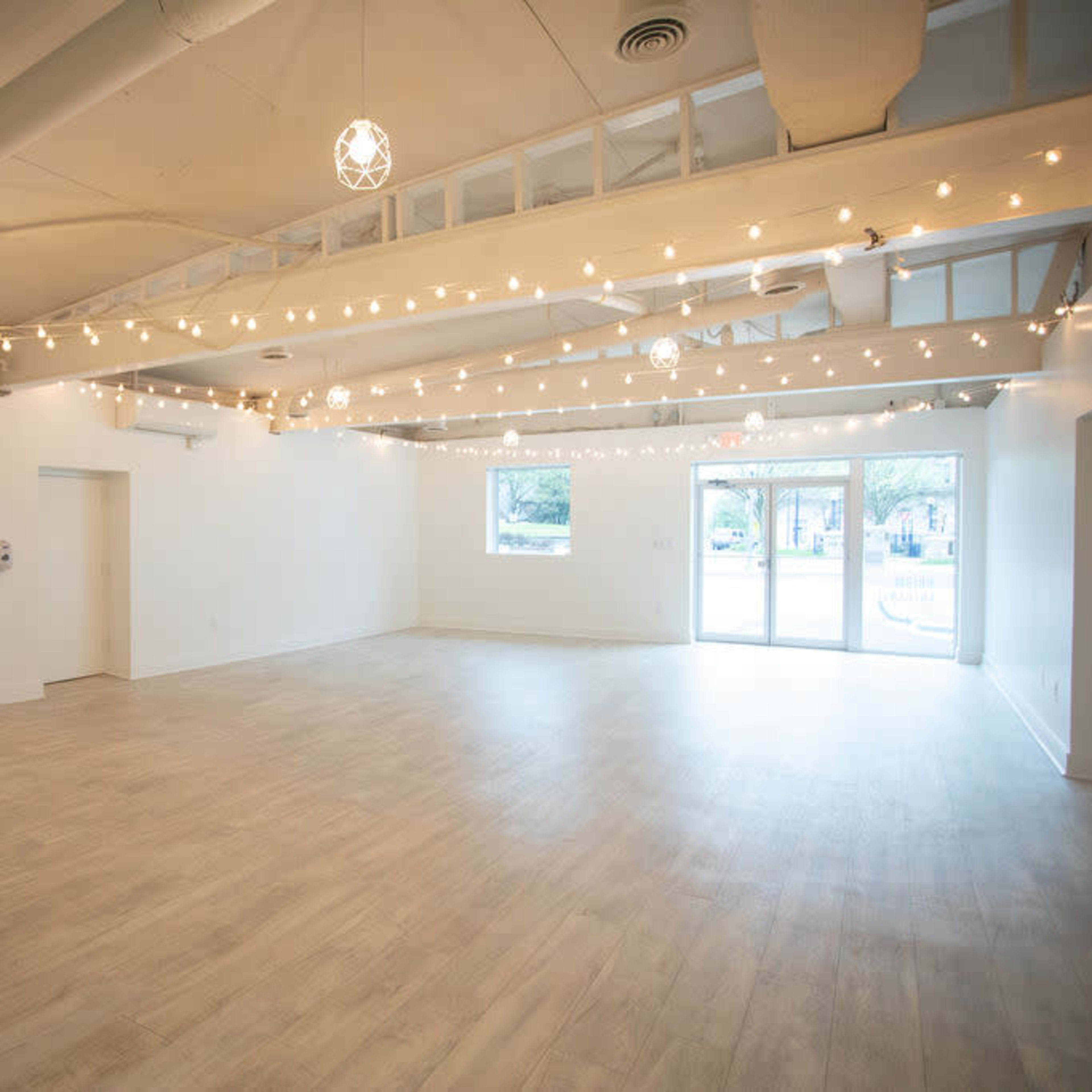 A spacious, empty room with light wooden flooring and string lights hanging from the ceiling.