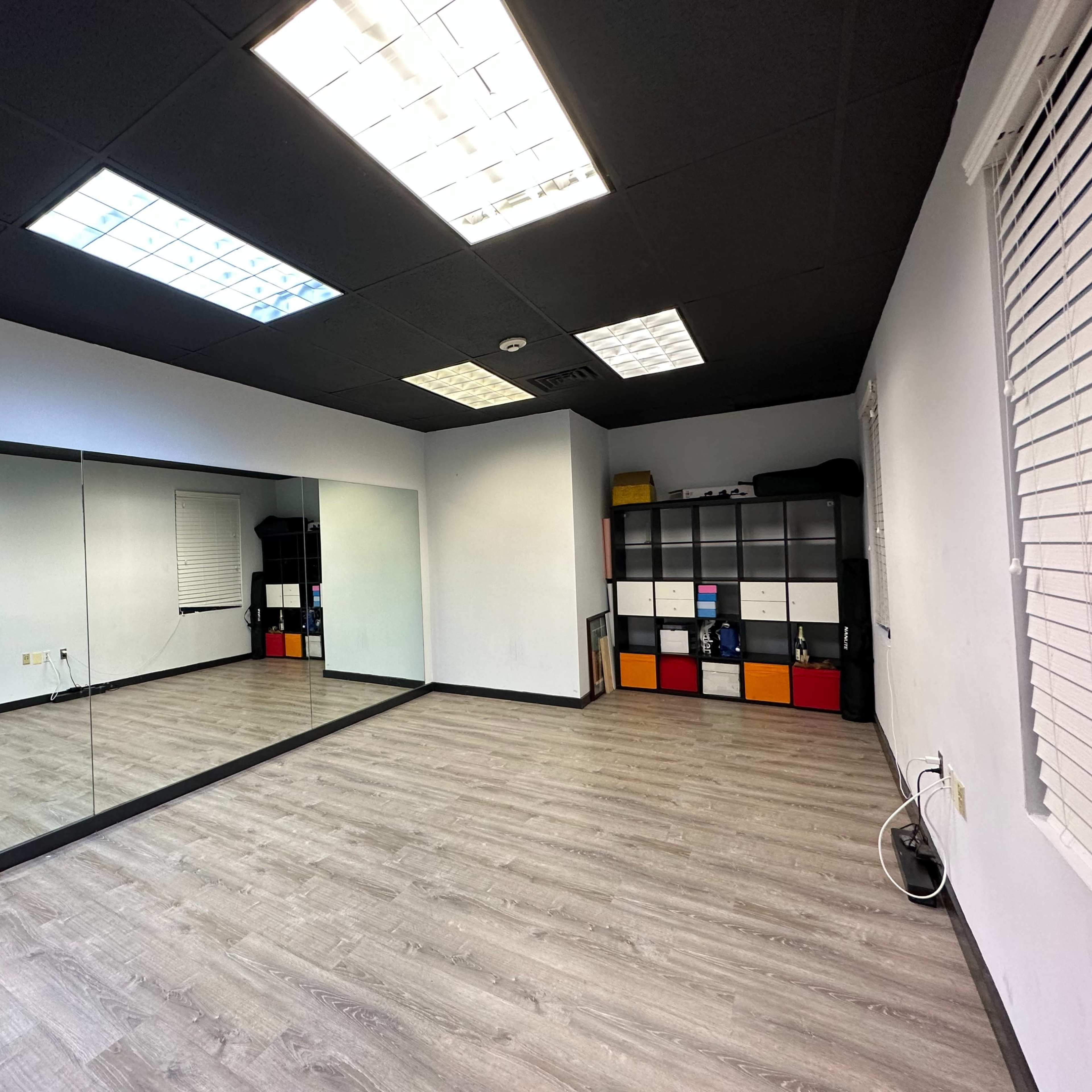 An empty room with a large mirror on one wall, gray flooring, and a set of black and white storage units against the opposite wall.