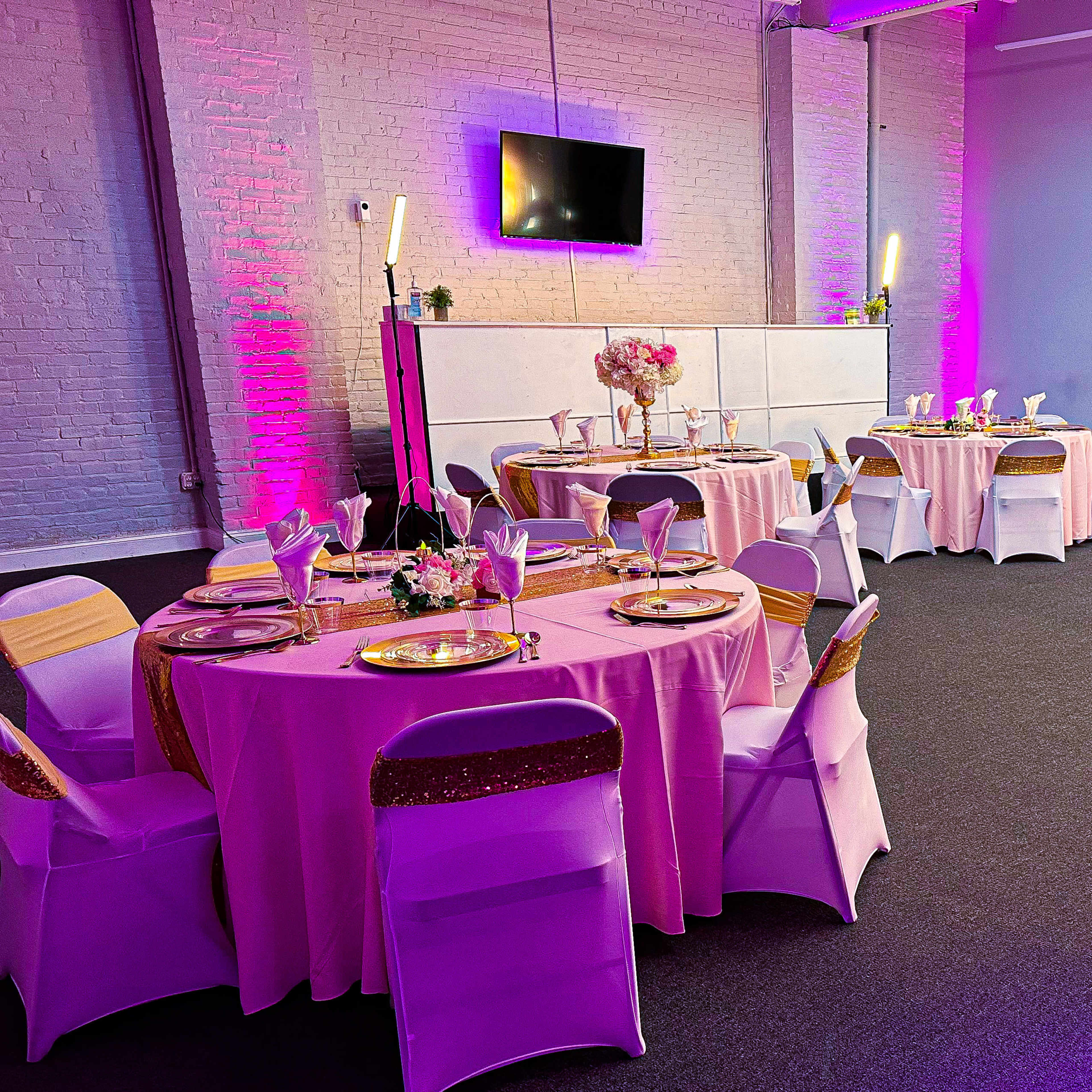 A decorated event space with several tables covered in pink tablecloths and white chairs, arranged for a gathering.