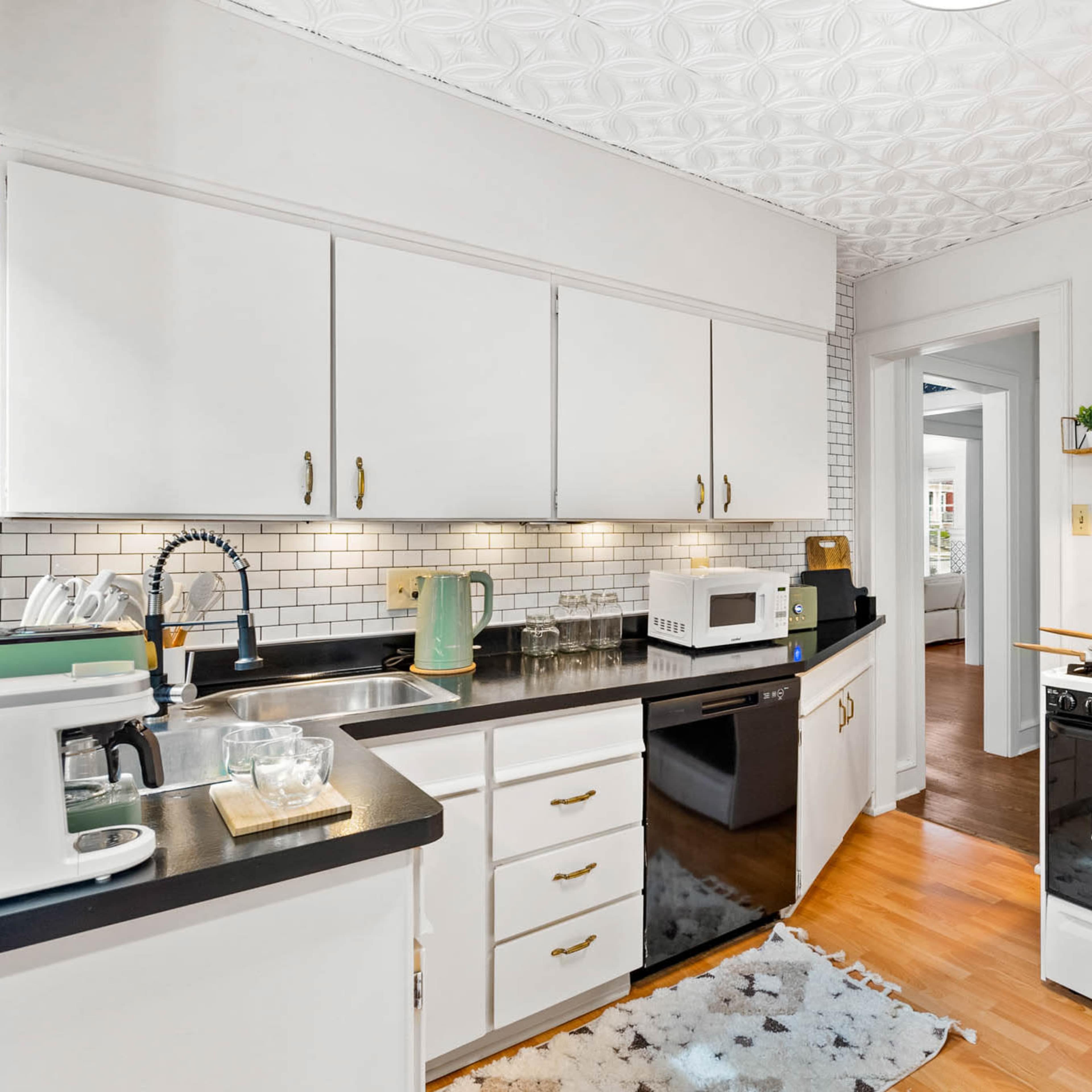 A modern kitchen features black countertops, white cabinets, a stove, and a microwave, with a small dining area visible through an archway.