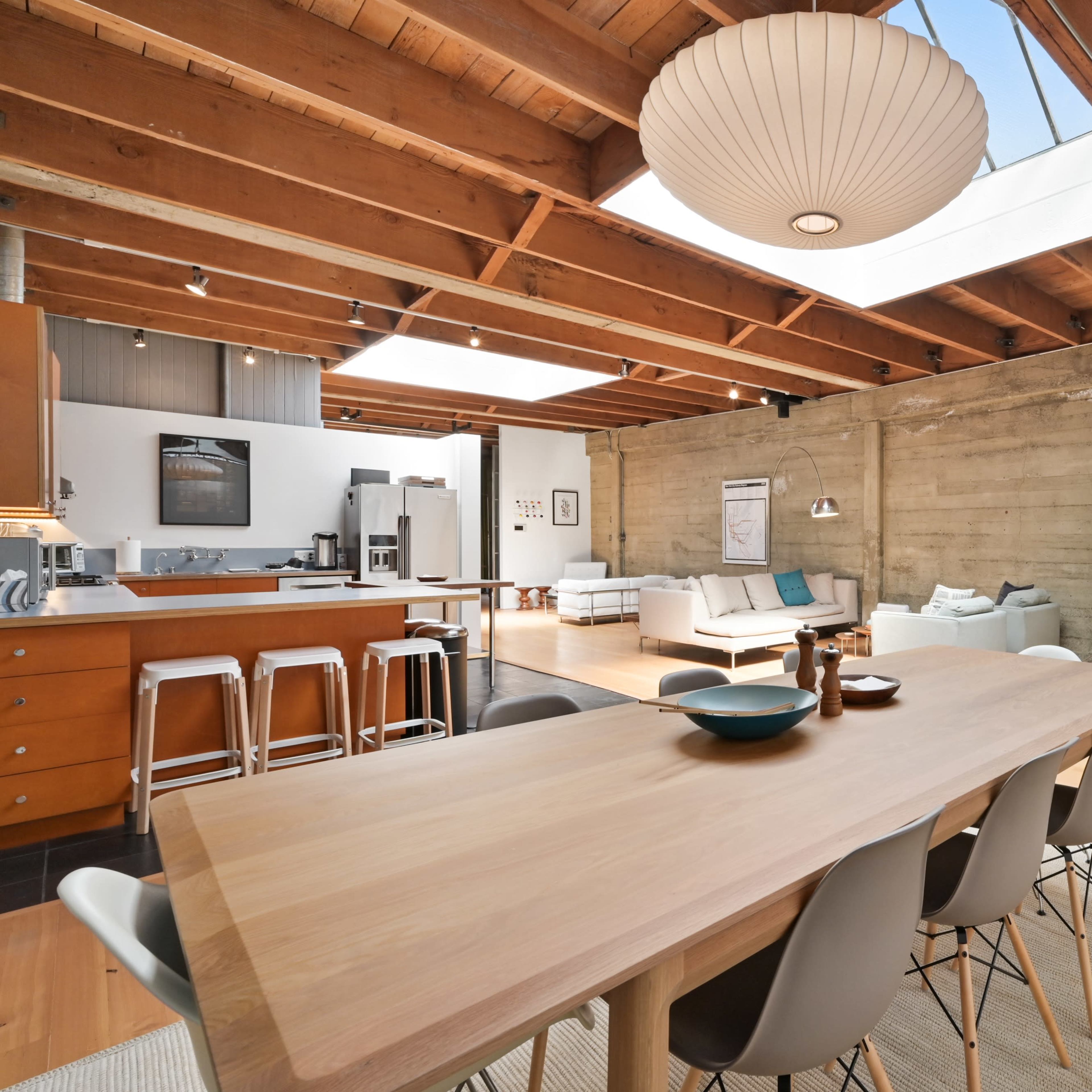 A spacious, modern open-concept living and dining area with wooden beams, a large dining table, and a bright seating area.