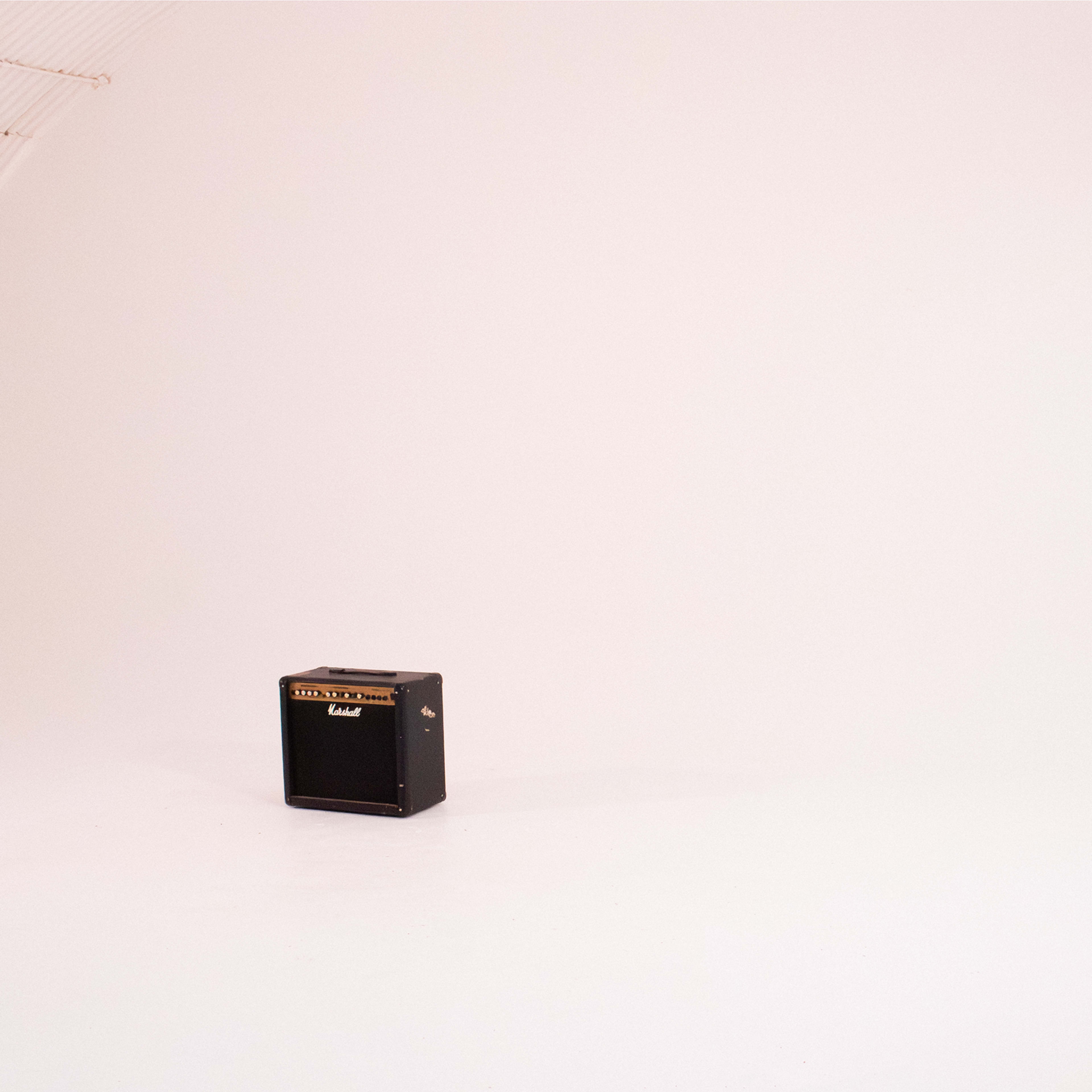 A black guitar amplifier positioned in a spacious, empty studio with white walls and a lighting setup on the right.