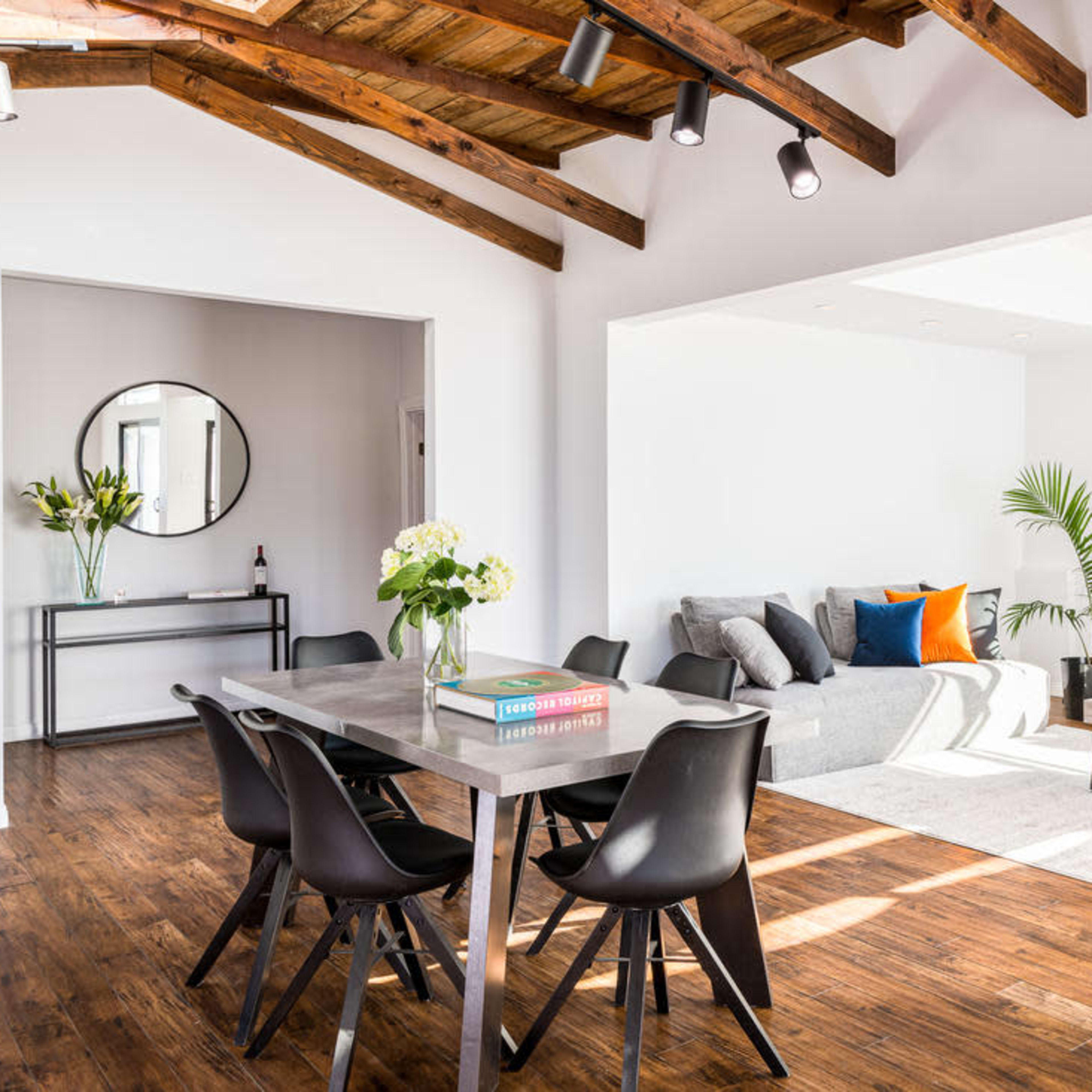 A modern open-concept living area with a dining table, chairs, and a seating area featuring a gray sofa and decorative pillows.