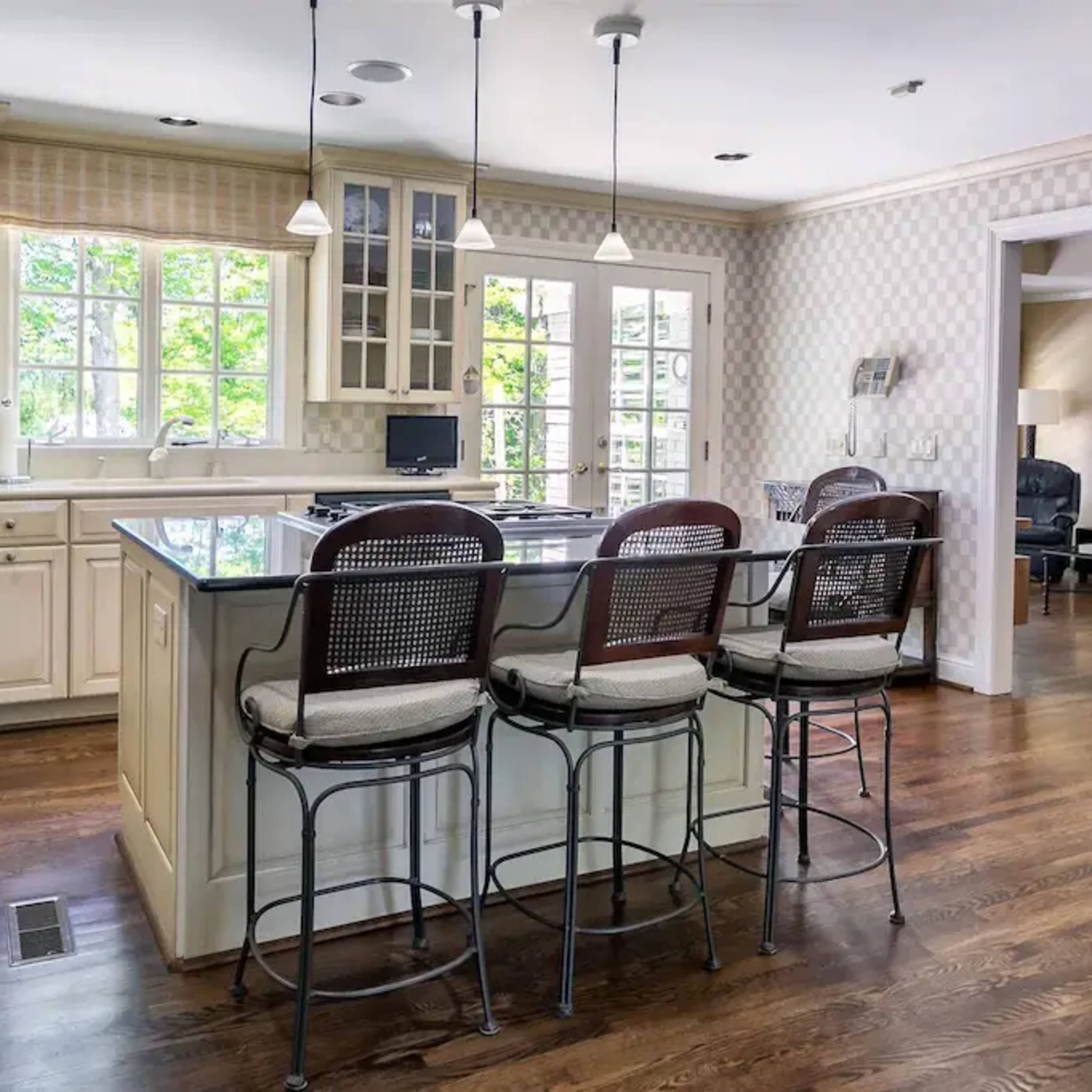 A modern kitchen with an island and barstool seating, adjacent to a living area with a sofa and decorative artwork.