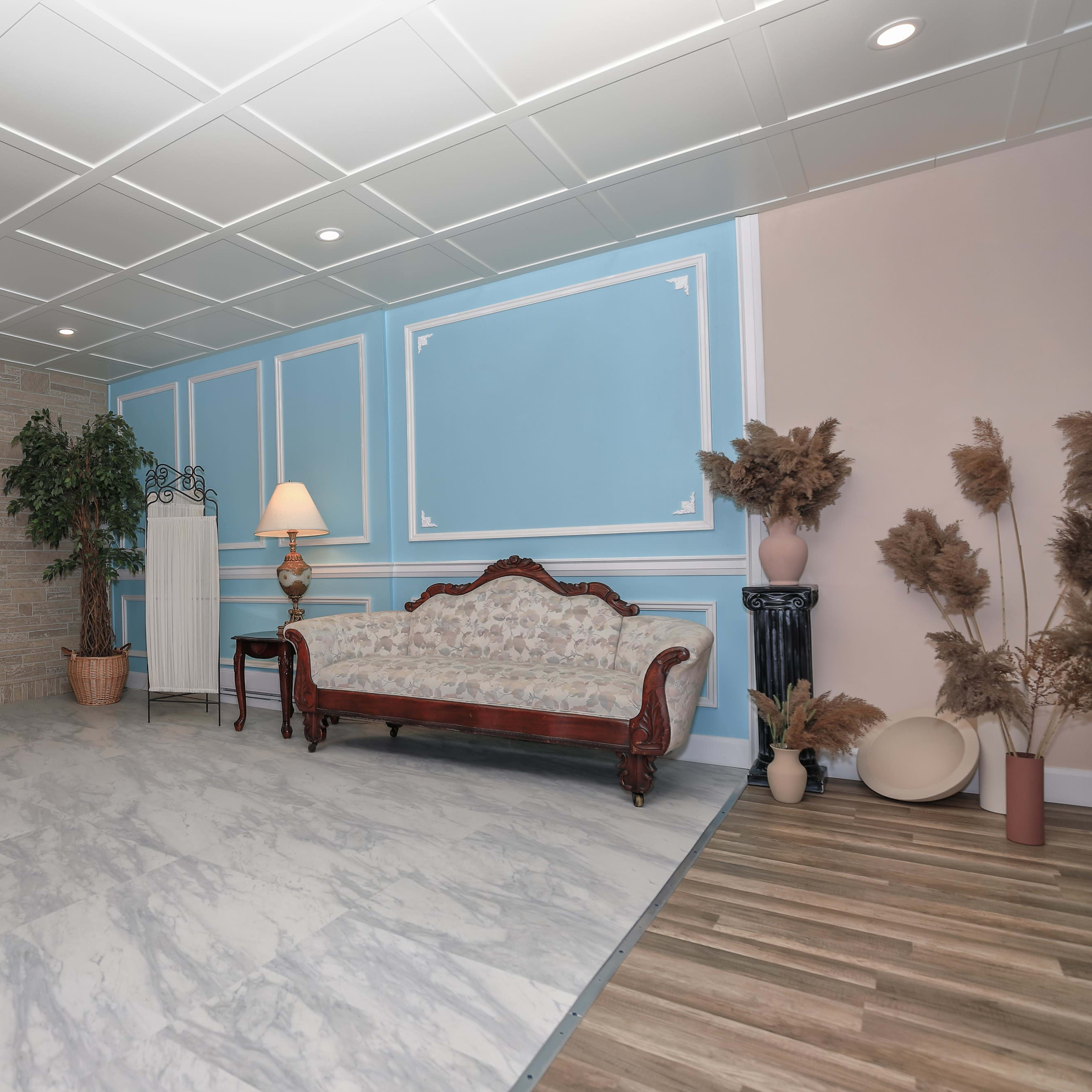 A spacious room with a patterned marble floor, a wooden reception area, a plush couch, and decorative plants against light-colored walls.