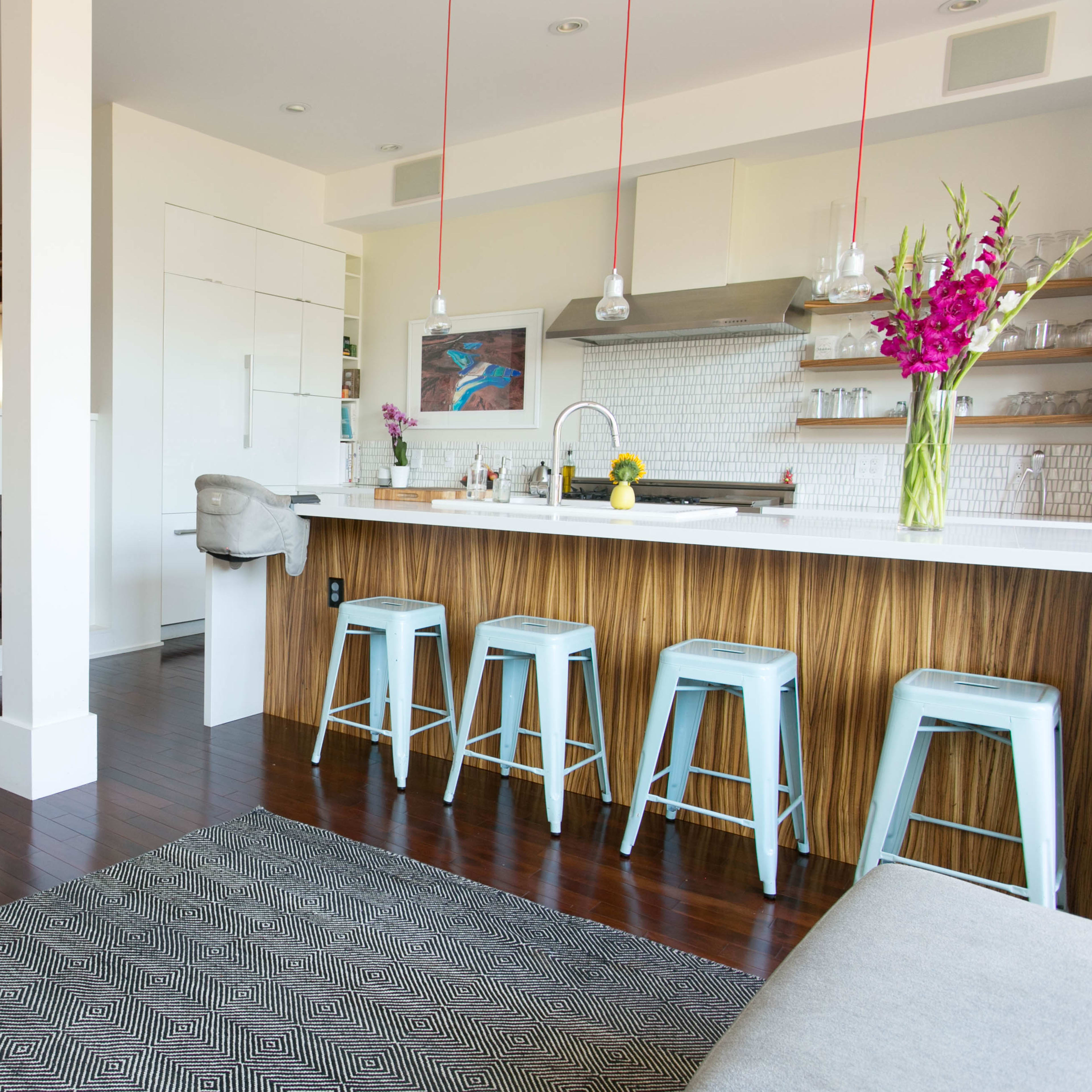 A modern open-concept living space featuring a kitchen with a bar, stools, and a fireplace, alongside a living area decorated with art and ambient lighting.