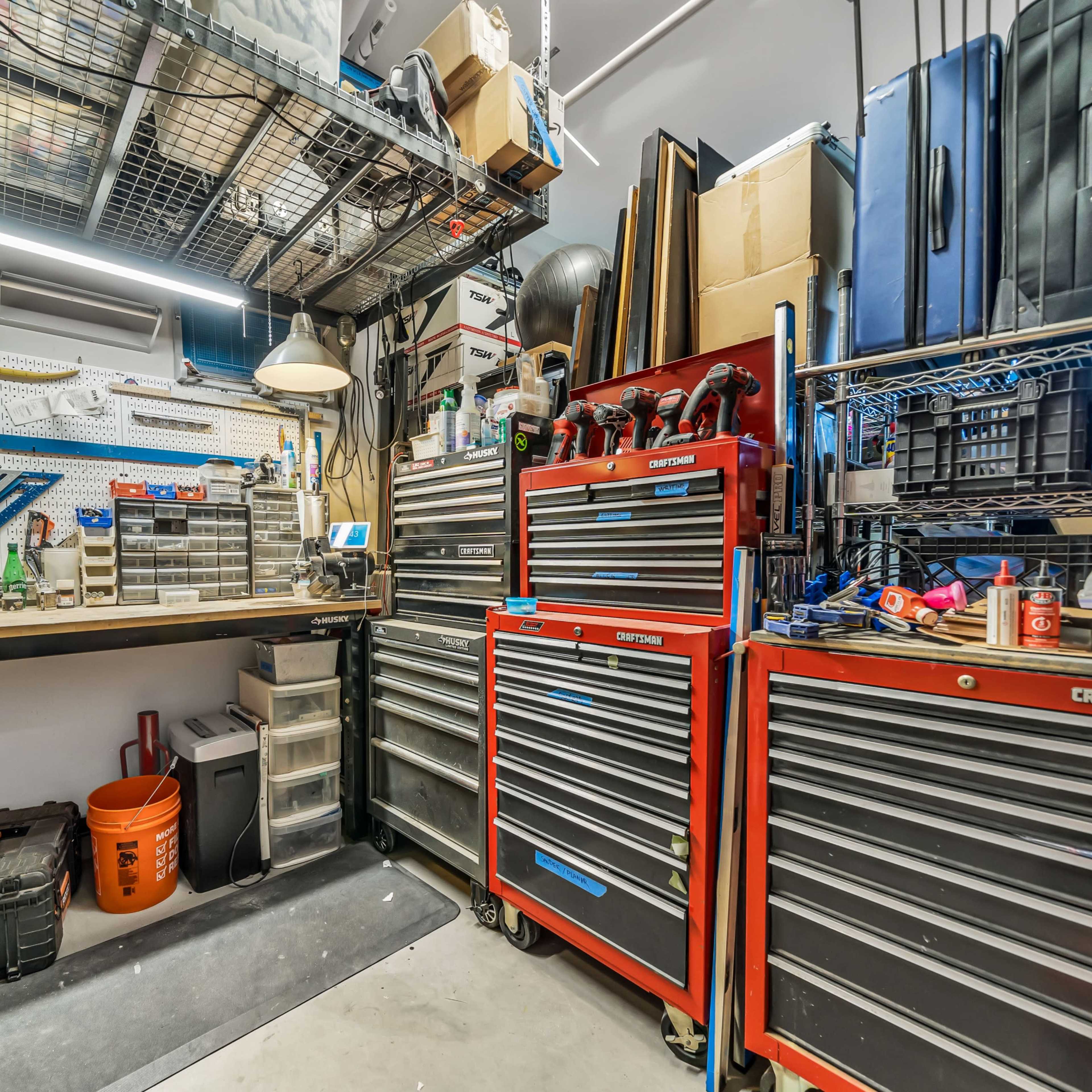 A well-organized garage workspace featuring tool chests, pegboards with various hand tools, and storage containers arranged along the walls.