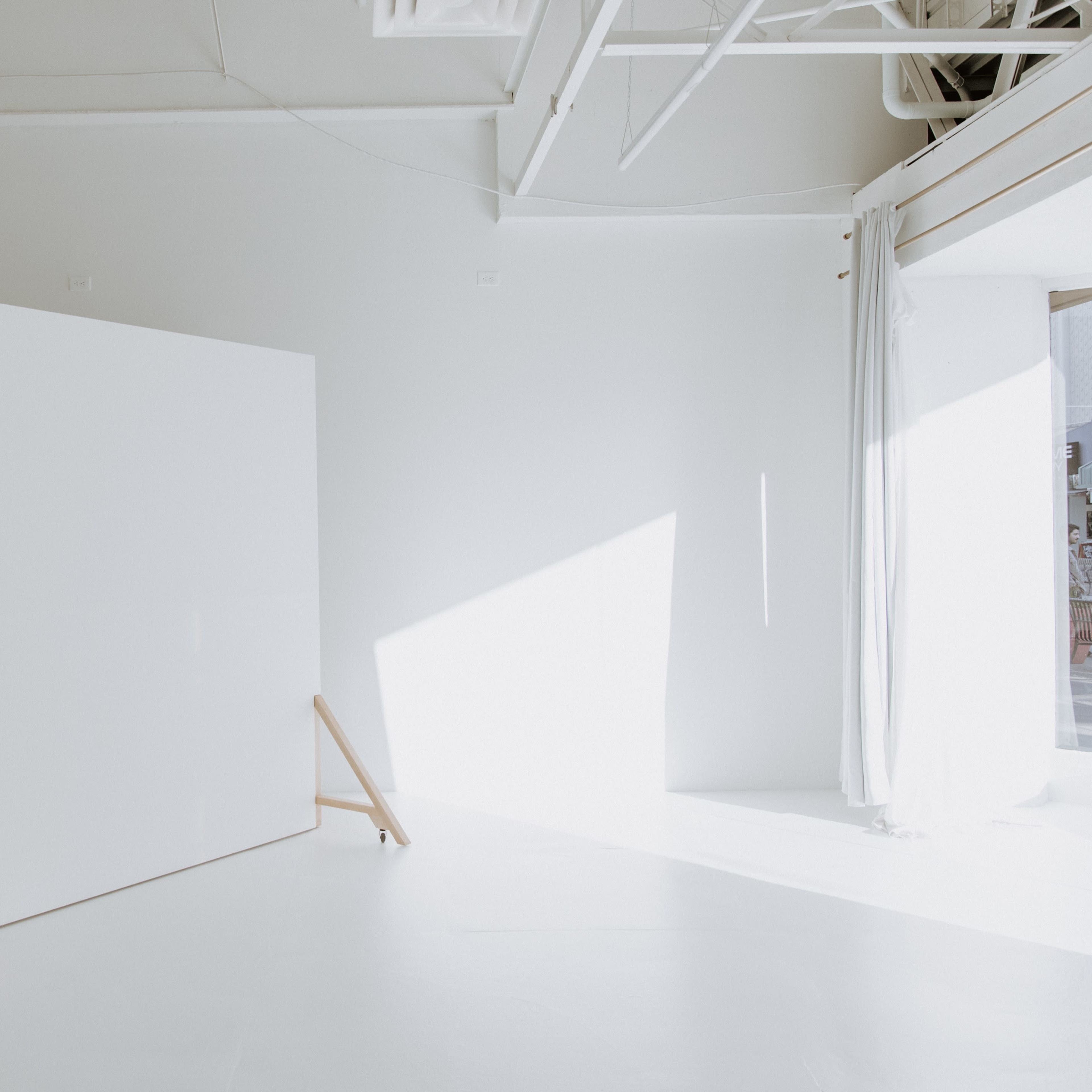 A large, blank white canvas stands on wooden support legs in a bright, minimalist studio space.